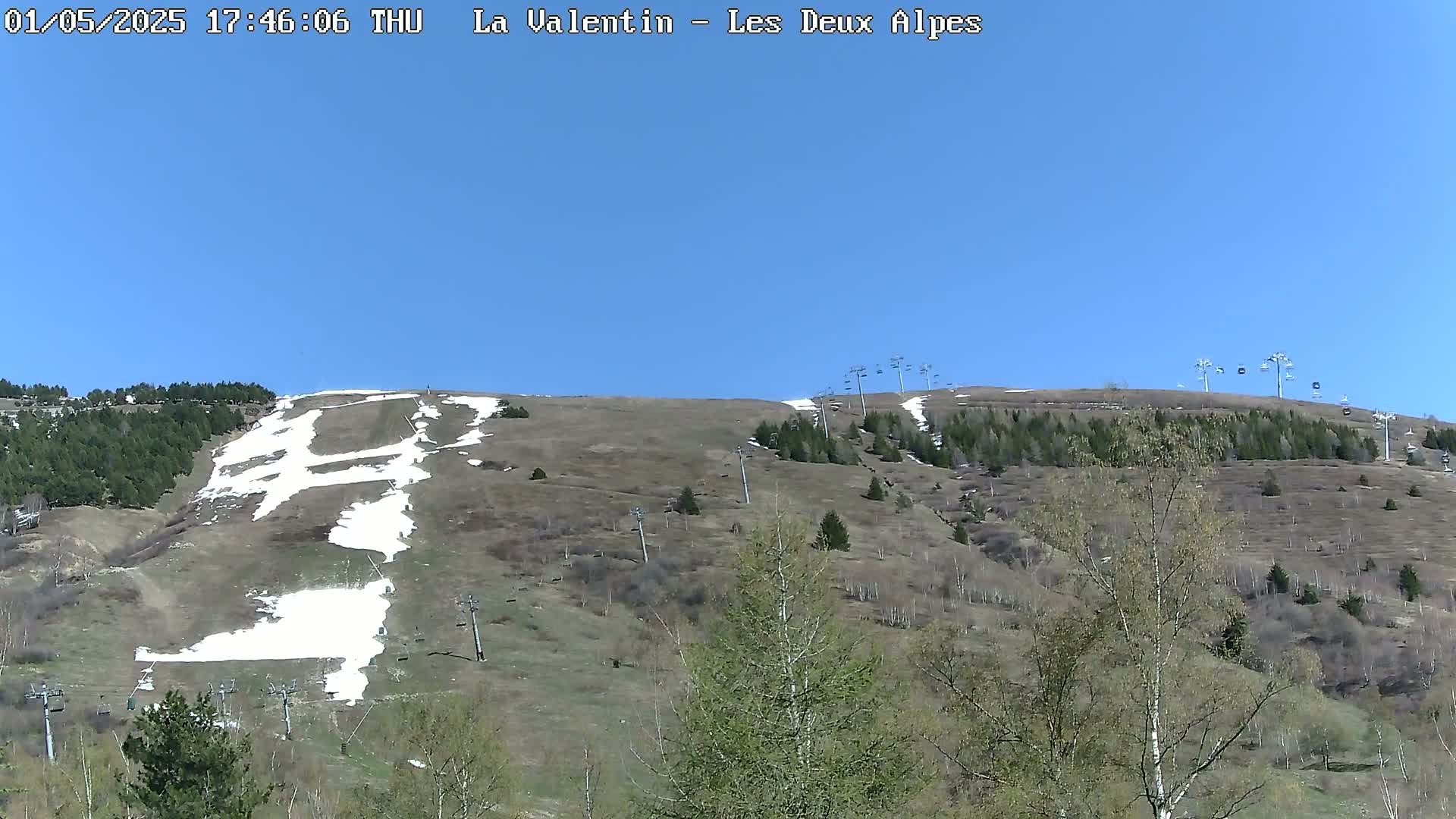 A mostly brown hillside with patches of snow and several chairlifts under a clear blue sky.