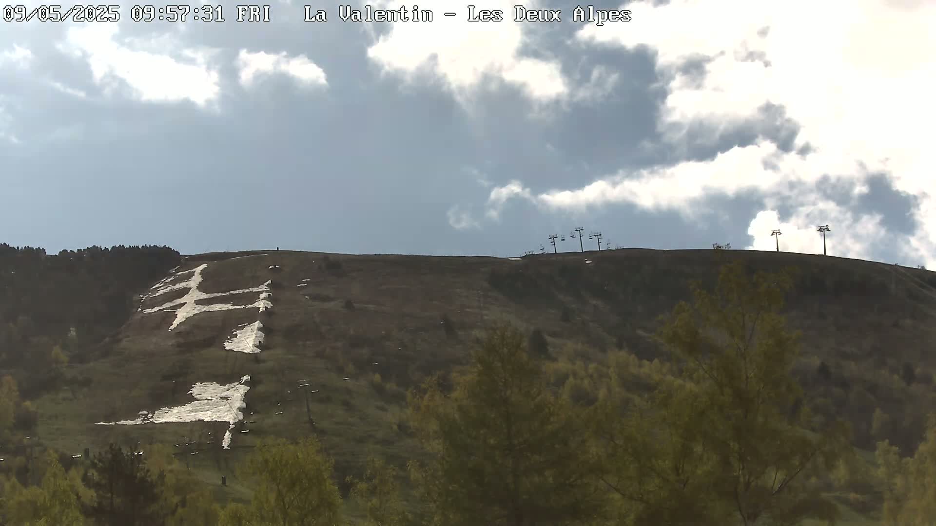 A partly cloudy sky overlooks a hillside with a large, painted cross and some sparse vegetation.