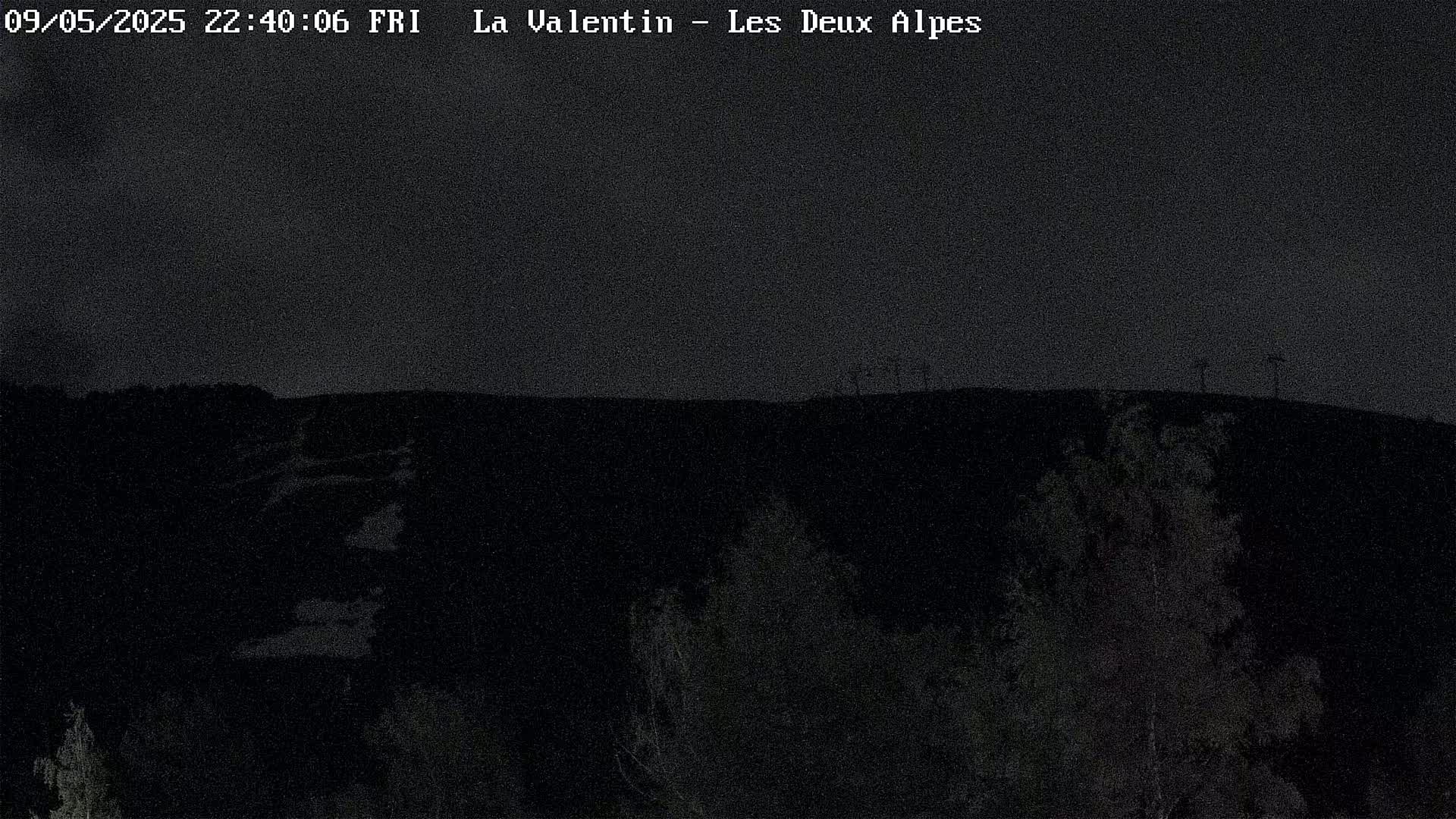 A nighttime view of a dark landscape with sparsely vegetated hills under a clear, dark sky.