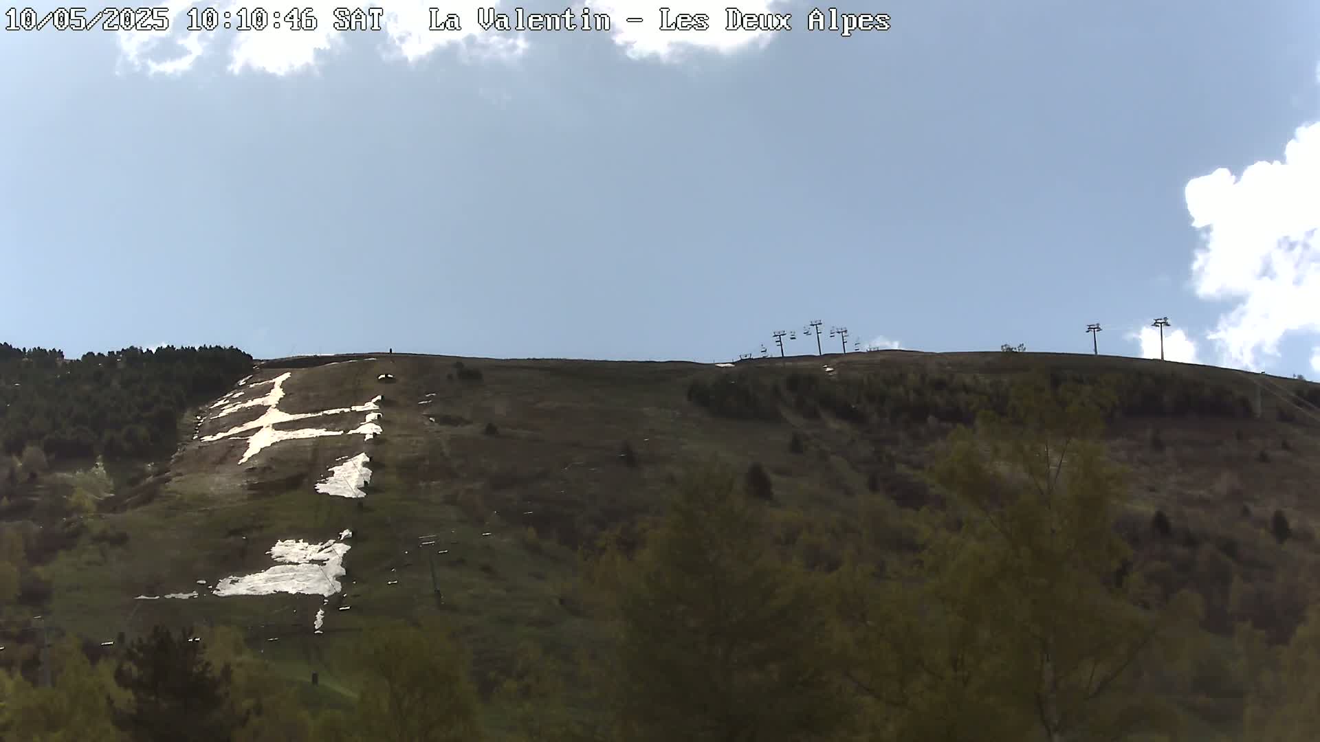 A mostly clear, blue sky is over a hillside with a large, white cross-shaped design in the snow, partially melted, near the top.