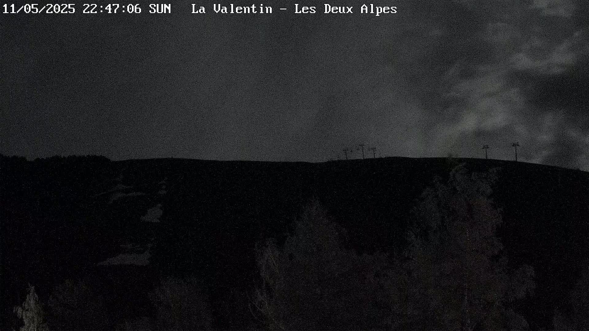 A dark, nighttime view of a hilltop with a few structures silhouetted against a cloudy sky.