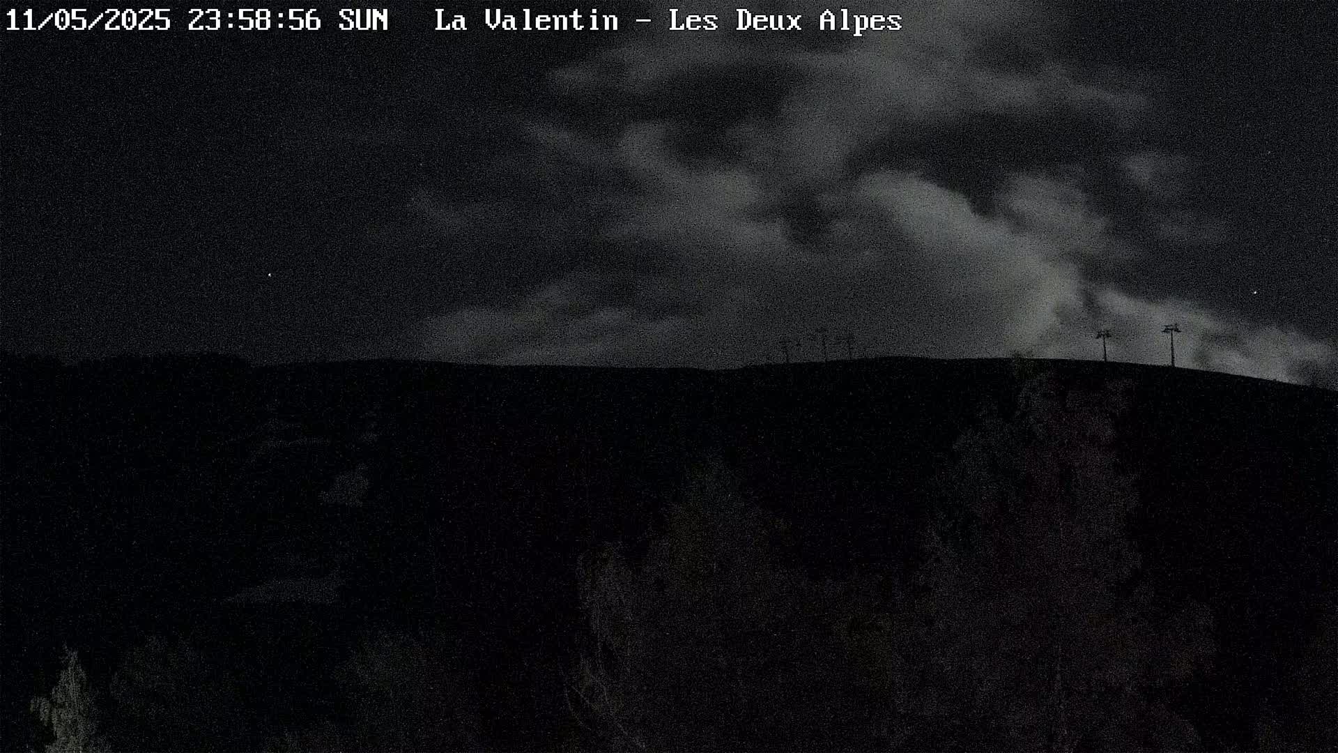 A dark, nighttime landscape shows a hilltop silhouetted against a cloudy sky.