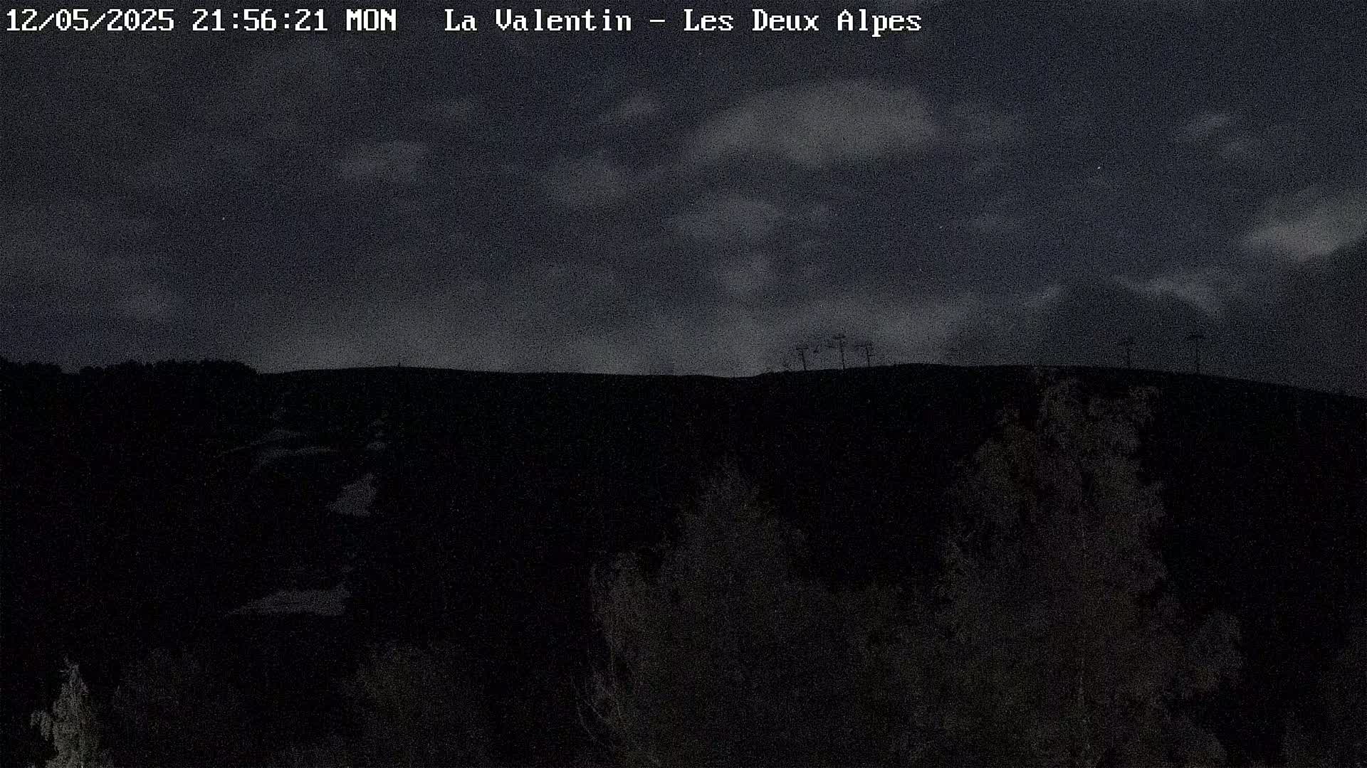 A dark, nighttime landscape shows a hilltop silhouetted against a cloudy sky.