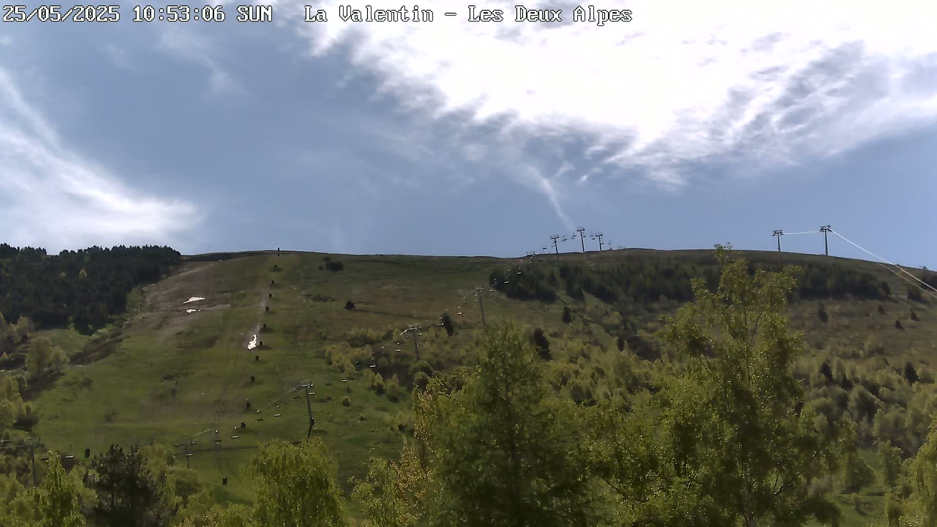 A grassy hillside dotted with trees and a chairlift under a partly cloudy sky.