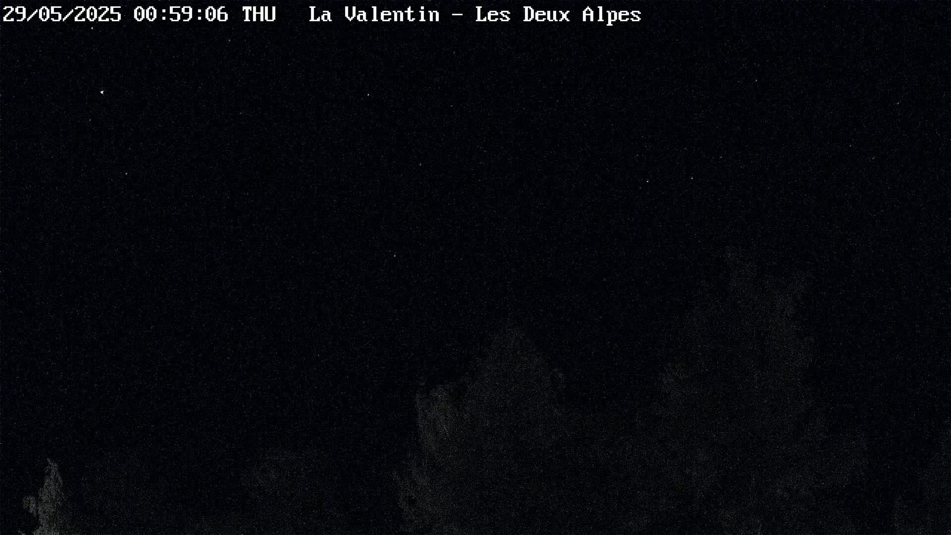 A nighttime, dark image shows a mostly clear sky with a few faint, distant lights or stars, and a dark, indistinct foreground.