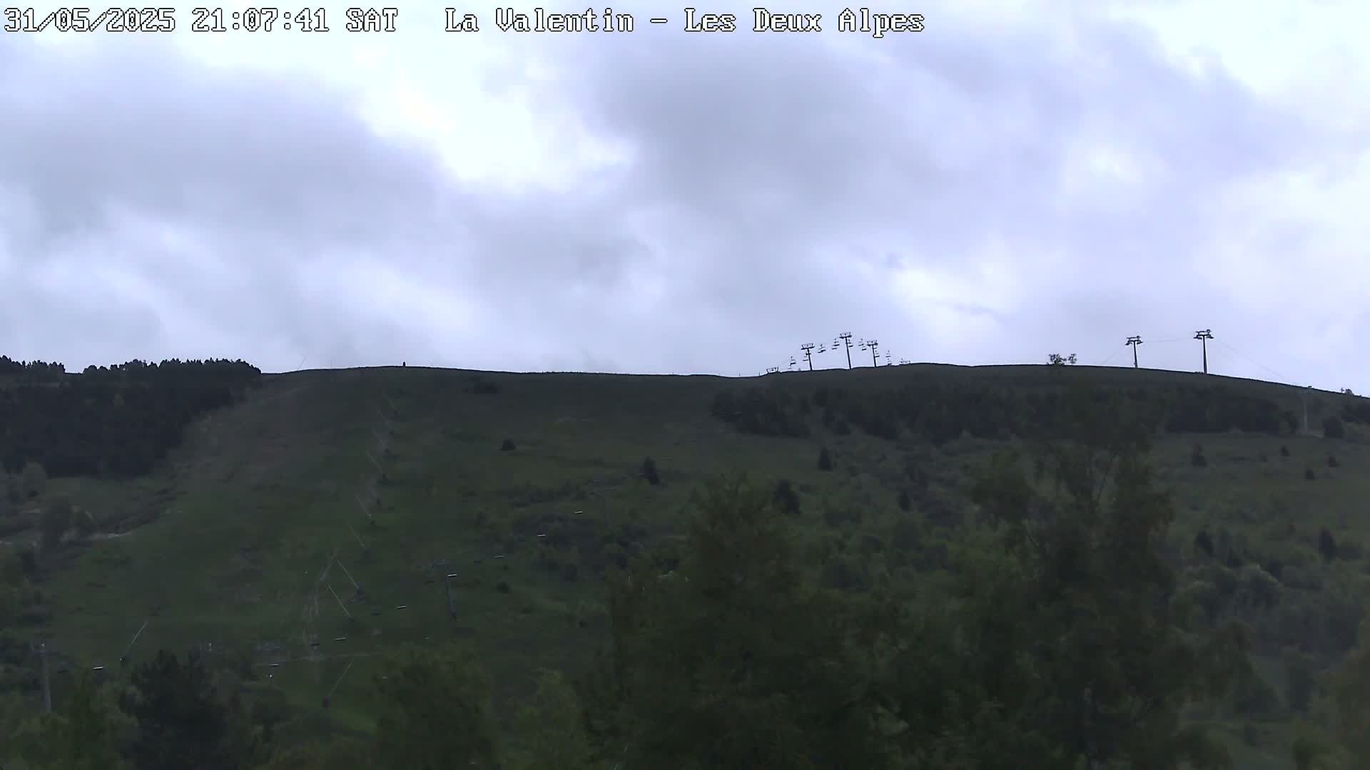 A grassy hill with ski lifts visible against a cloudy sky.