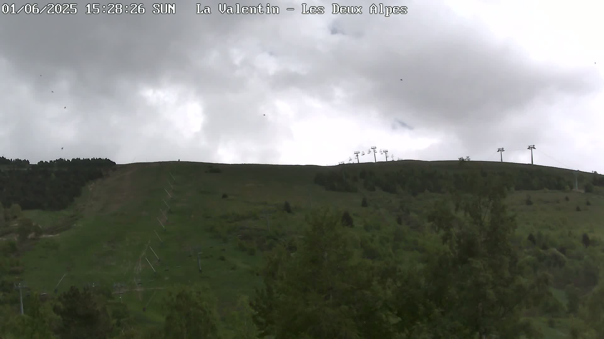 A grassy hillside with a few ski lifts is visible under an overcast sky.