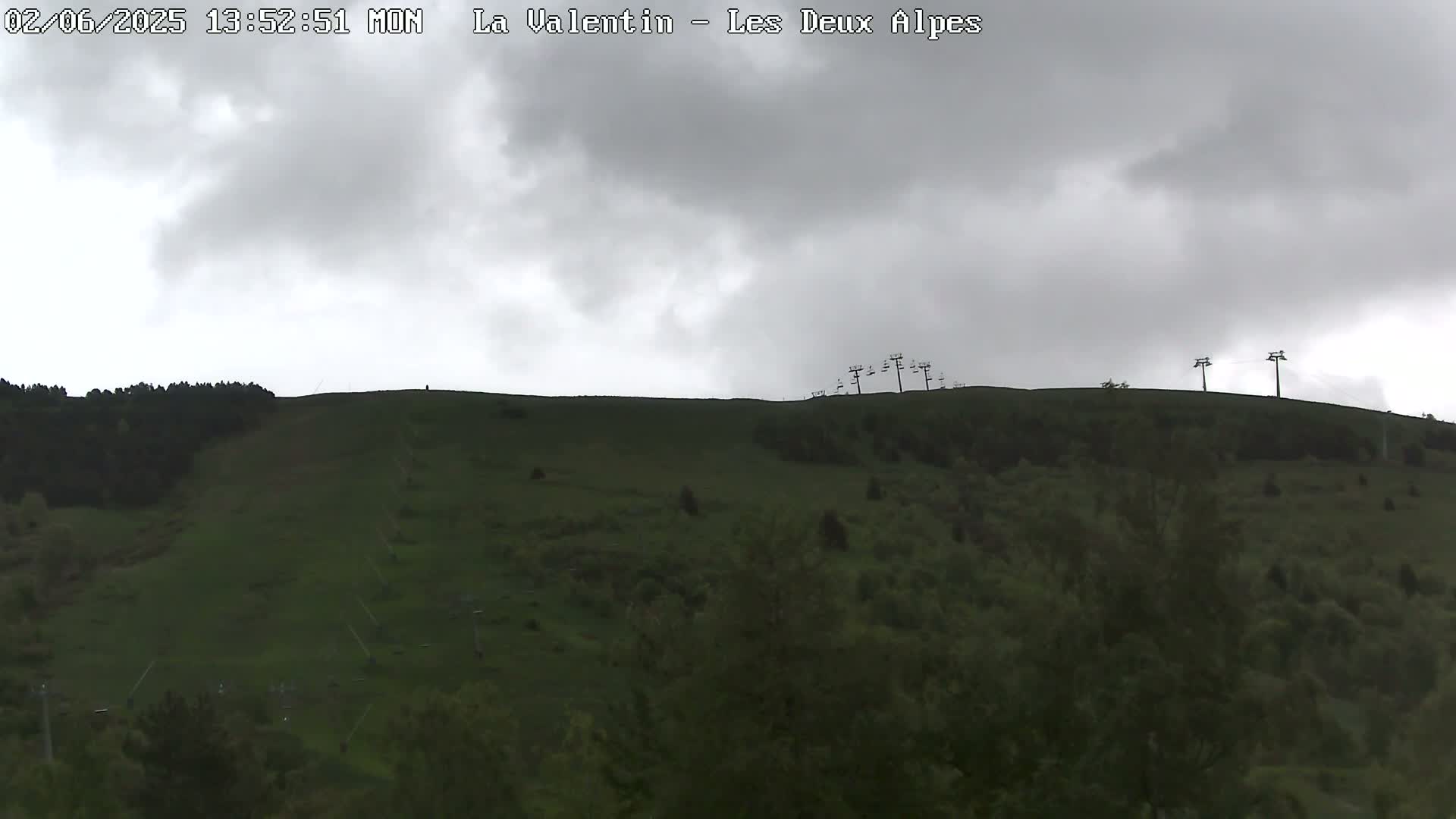A grassy hillside with sparsely spaced trees and several chairlift towers is visible under an overcast sky.