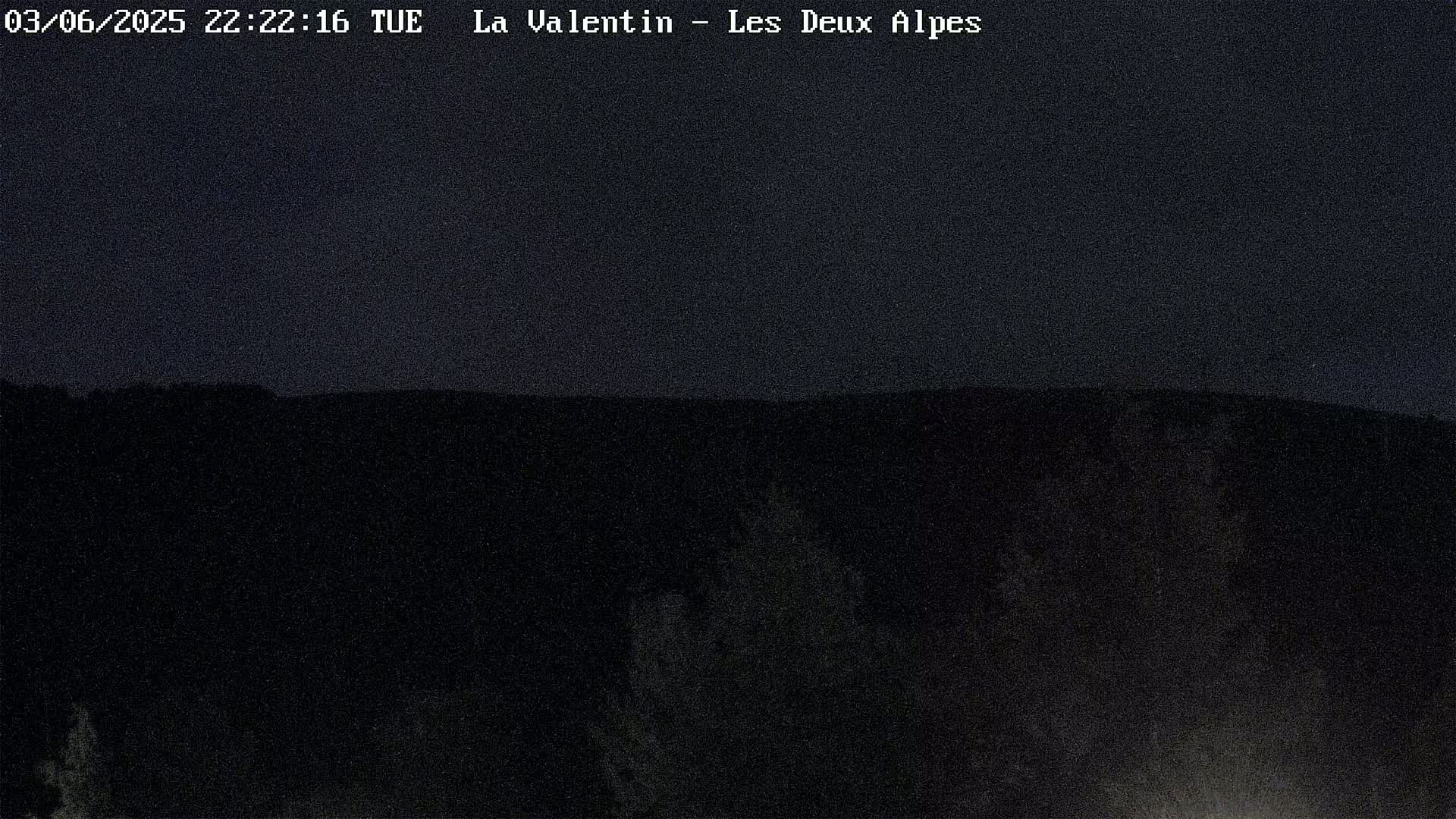 A dark nighttime view of a mountainous landscape under a clear sky.