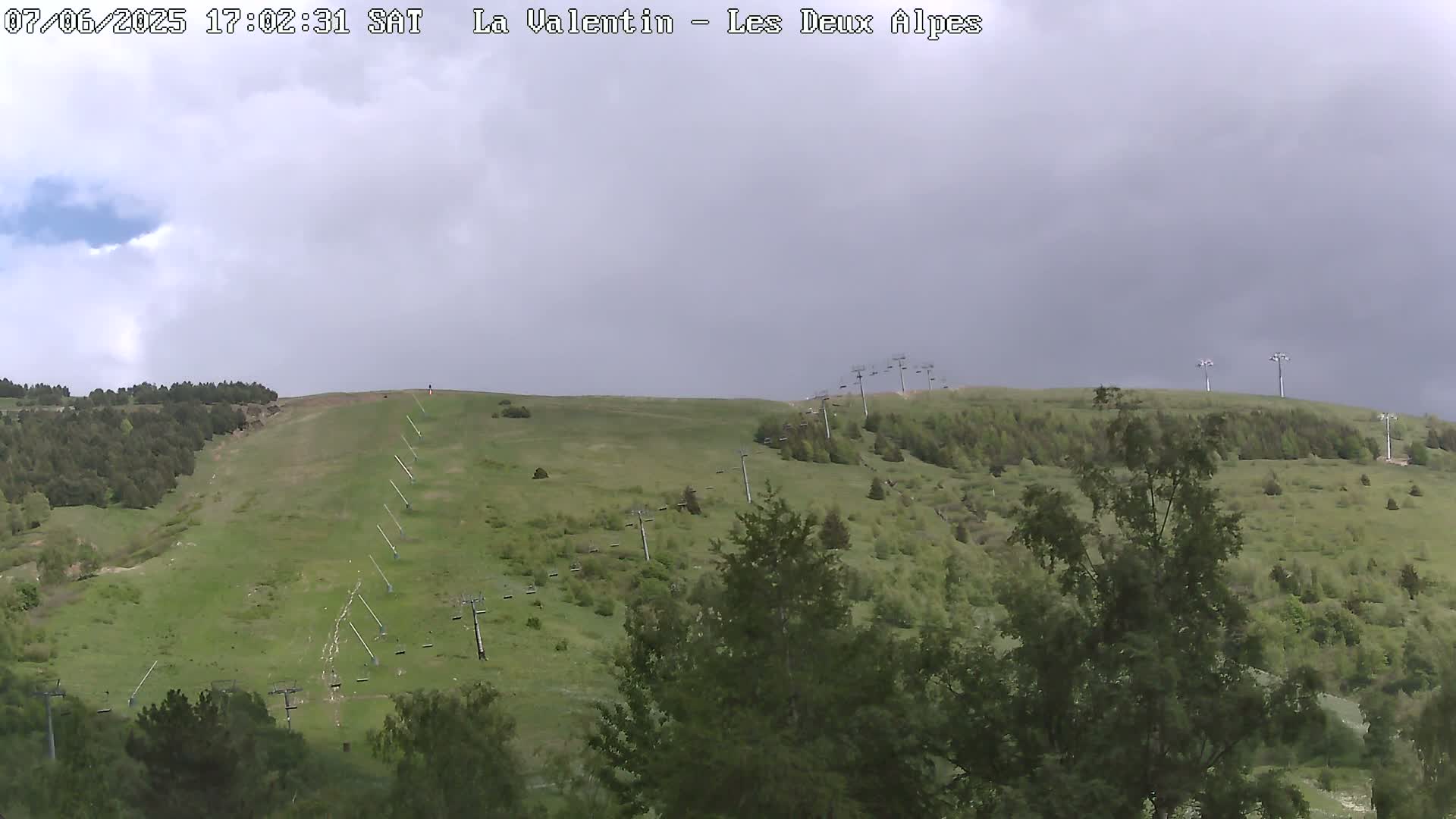 A grassy hillside with several chairlifts under an overcast sky.