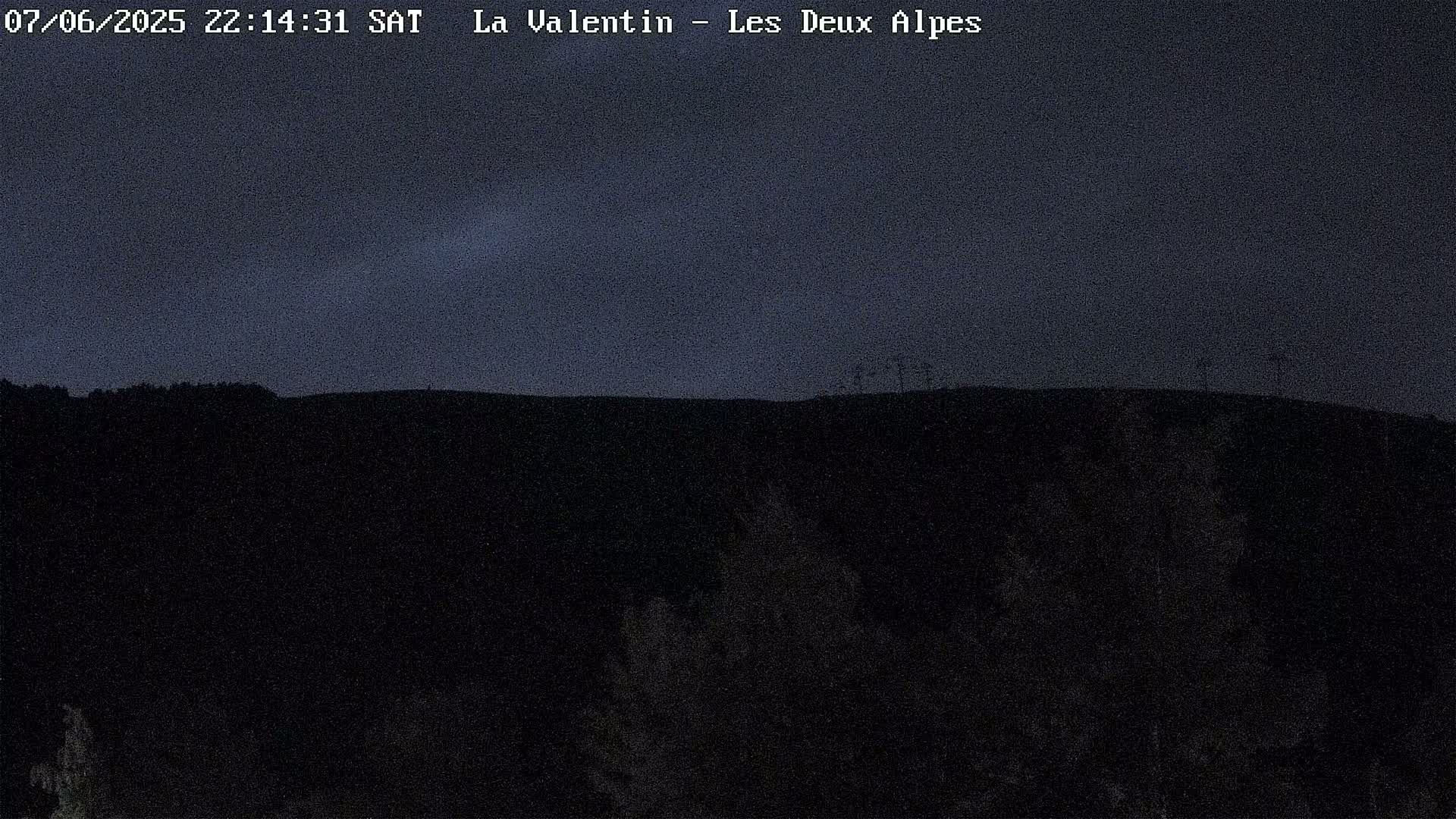A nighttime view of a dark, hilly landscape under a mostly clear, dark blue sky.