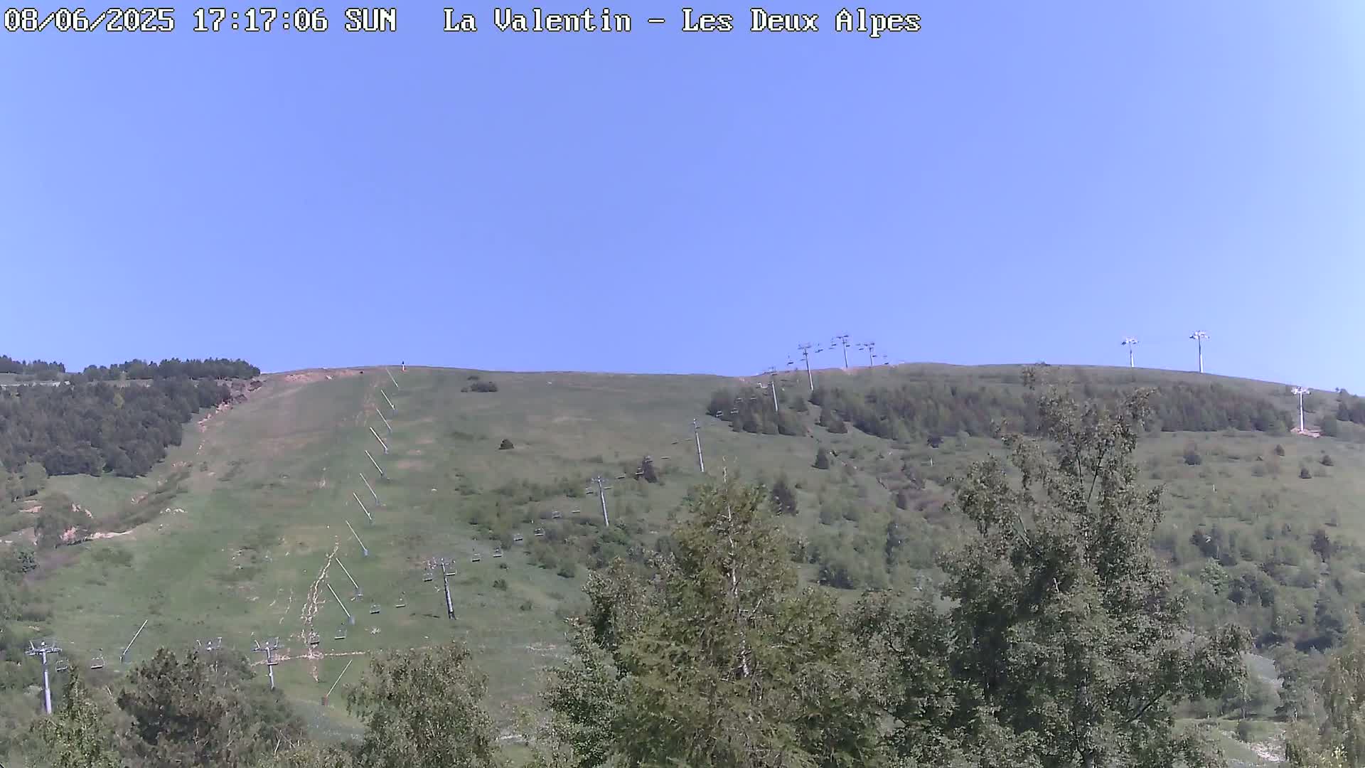 A grassy hillside with several chairlifts visible under a clear blue sky.