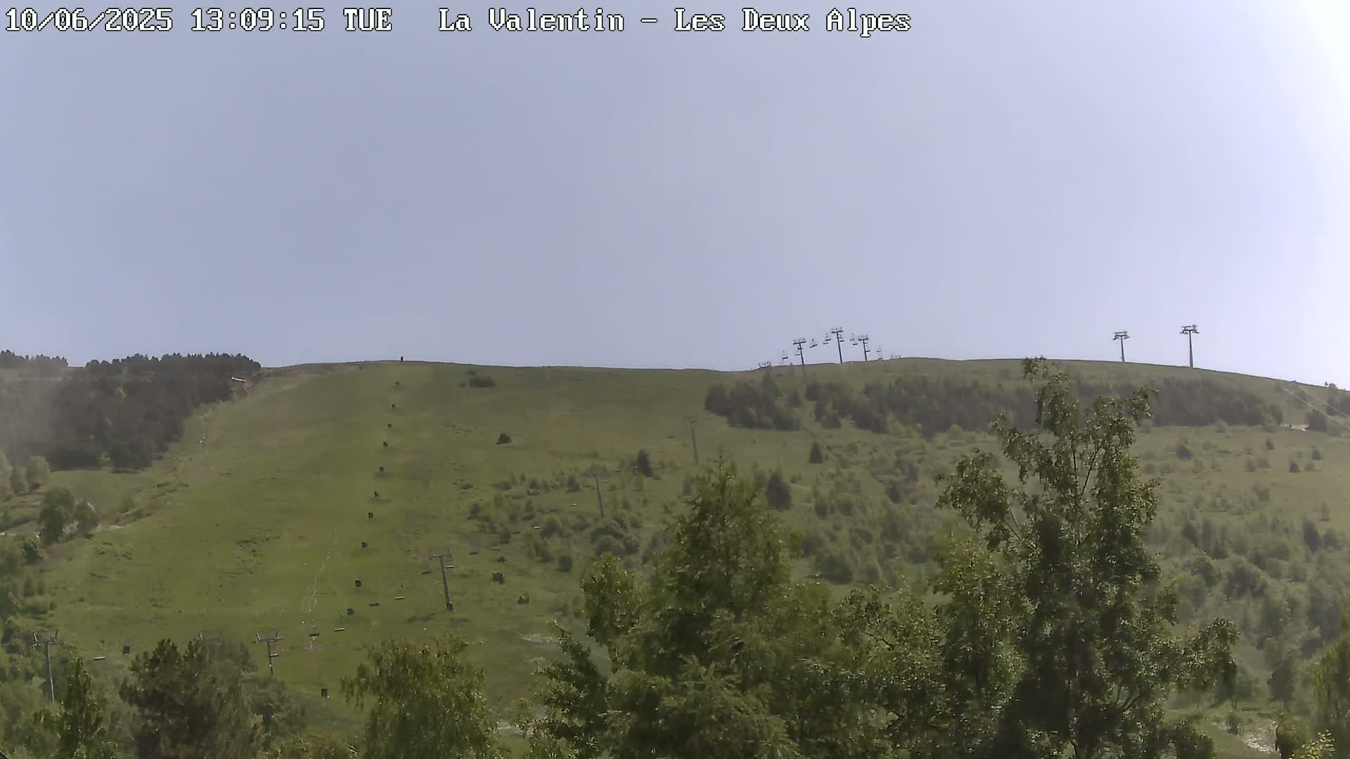 A grassy hillside with sparse trees and chairlifts under a clear, light-blue sky.