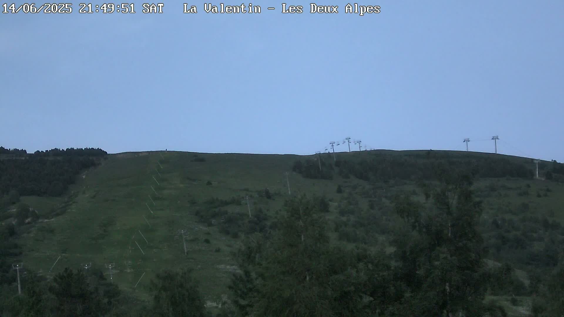 A grassy hillside with several chairlifts under a cloudy sky.