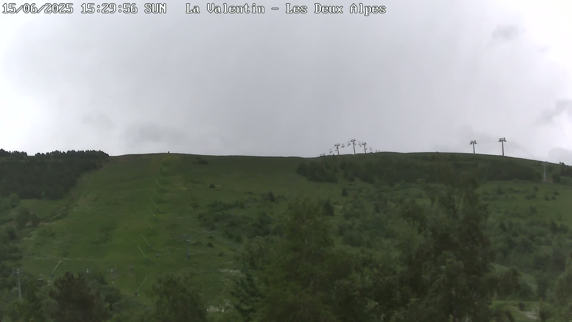 A mostly overcast sky overlooks a grassy hillside with sparsely wooded areas and several chairlifts.