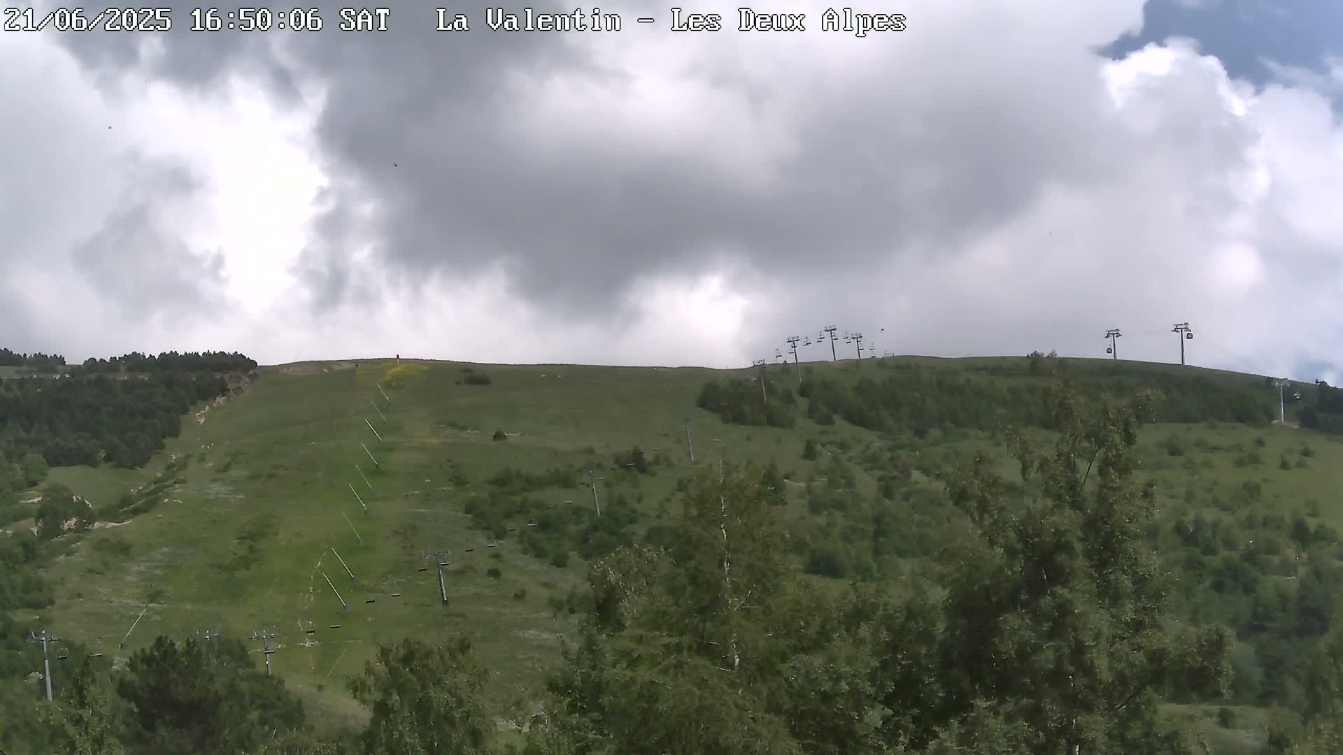 A grassy hillside with several chairlifts under a mostly cloudy sky.