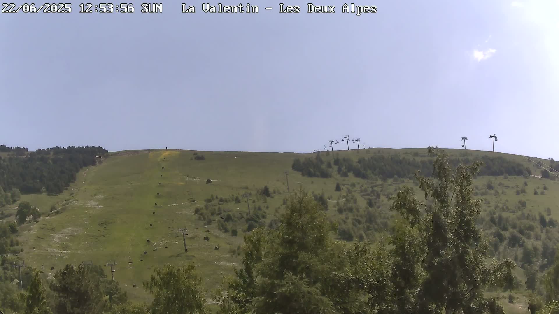 A sunny day reveals a grassy hillside dotted with trees and several chairlifts ascending towards the summit.