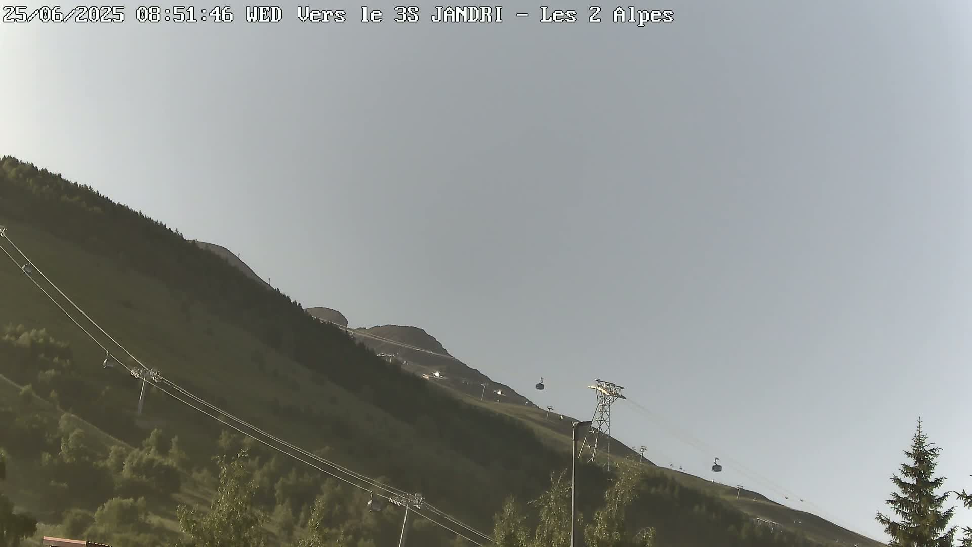 A chairlift ascends a grassy mountainside under a clear, light-grey sky.