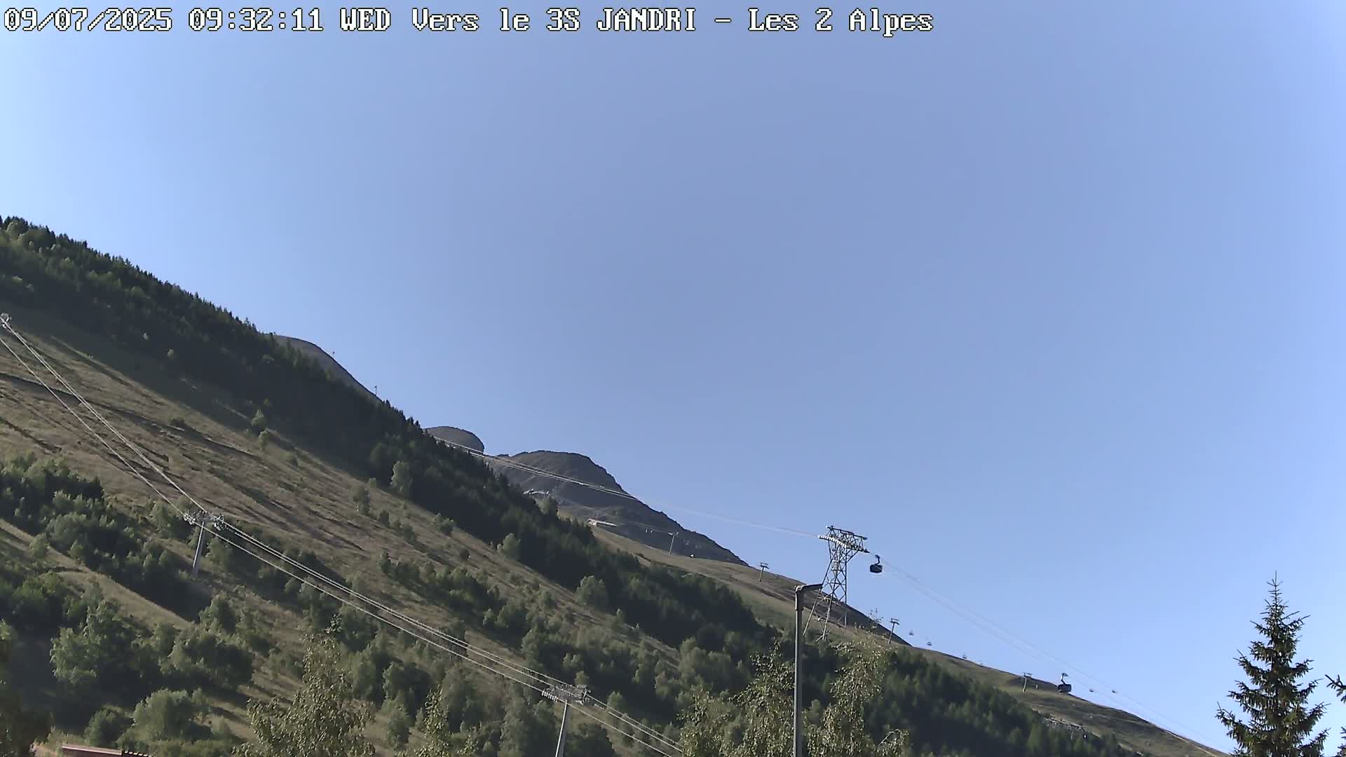 A mountain slope with sparse vegetation and a chairlift under a clear blue sky.