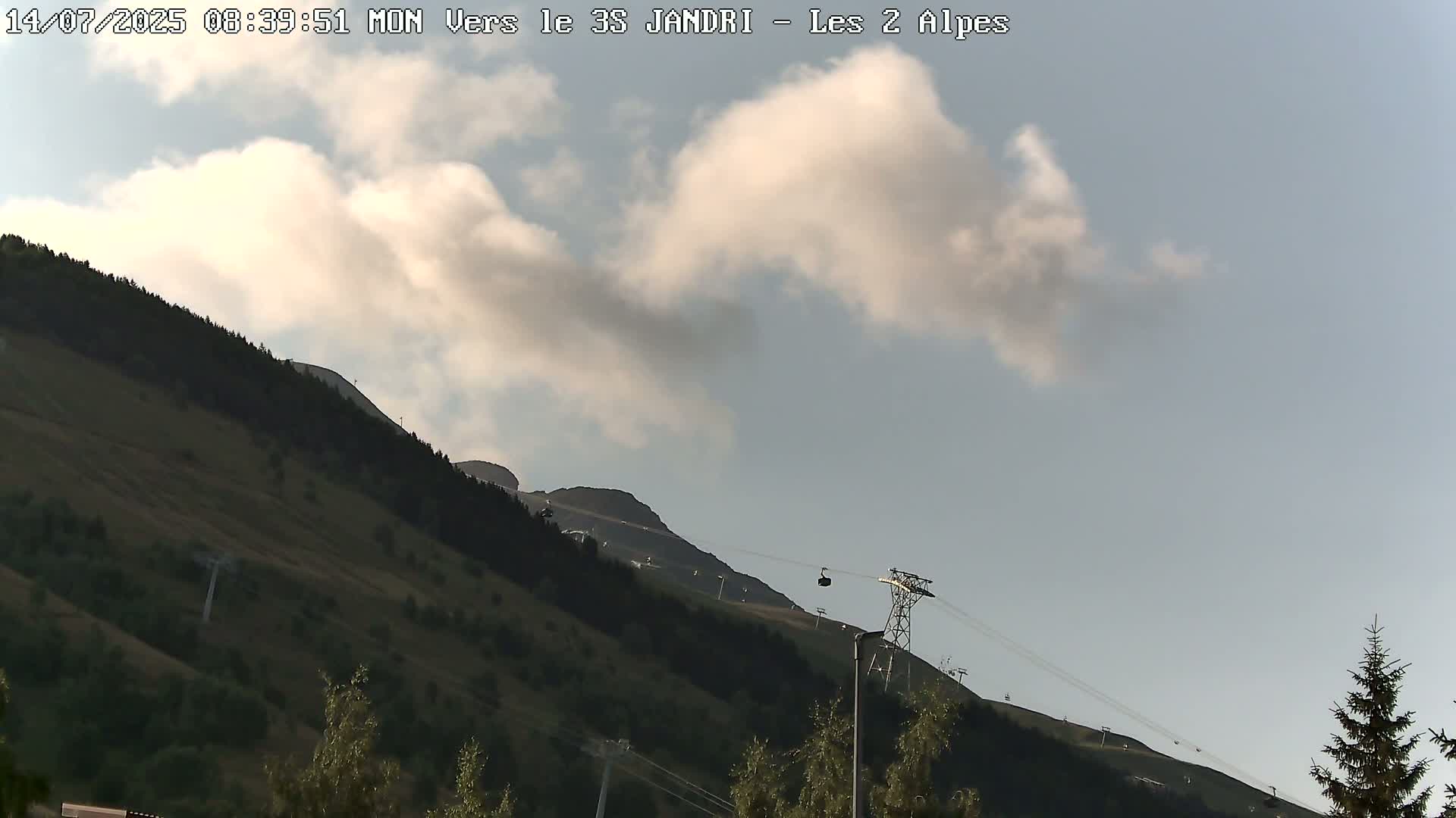A partly cloudy sky overlooks a grassy mountainside with a chairlift and sparse trees.