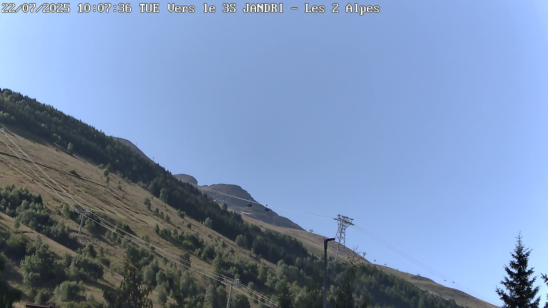 A clear blue sky overlooks a mountain slope with sparse vegetation and a cable car system.