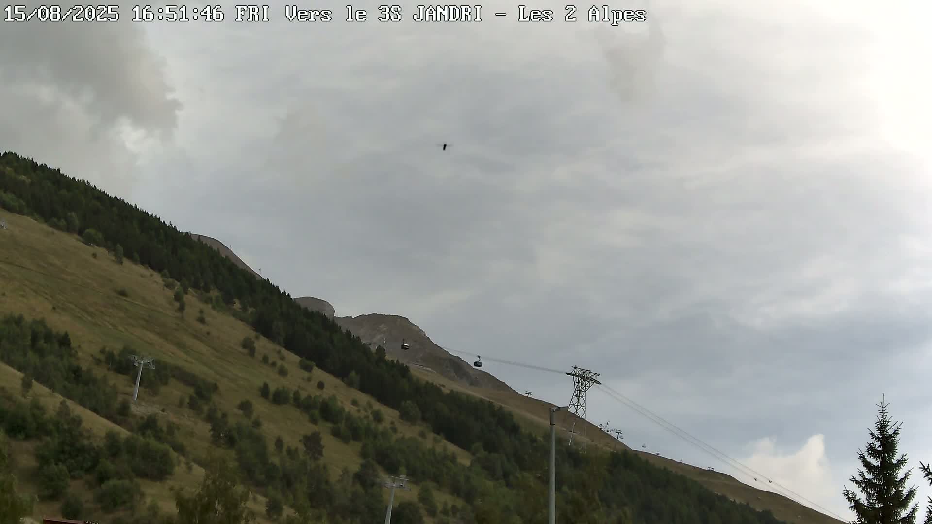 A clear blue sky overlooks a mountain slope with sparse vegetation and a cable car system.