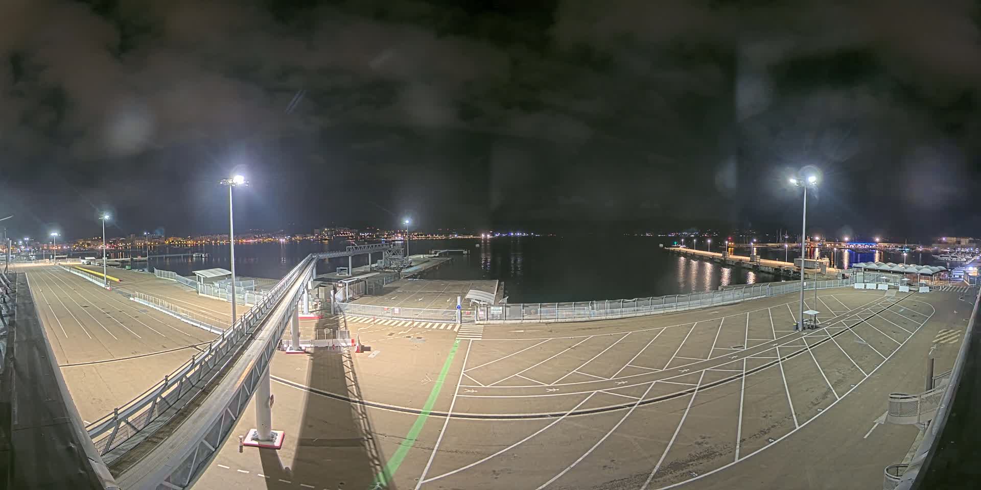 A nighttime view of an empty port area with a gangway leading to a dock, under a cloudy sky.