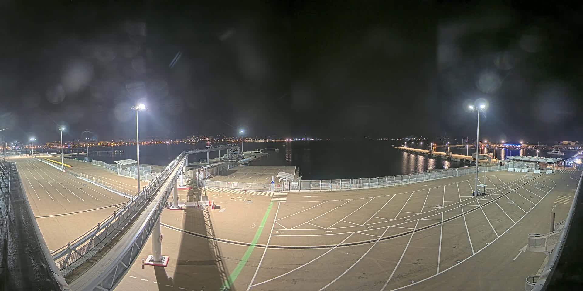 A nighttime view of an empty port area with a gangway leading to a dock, under a slightly hazy sky.