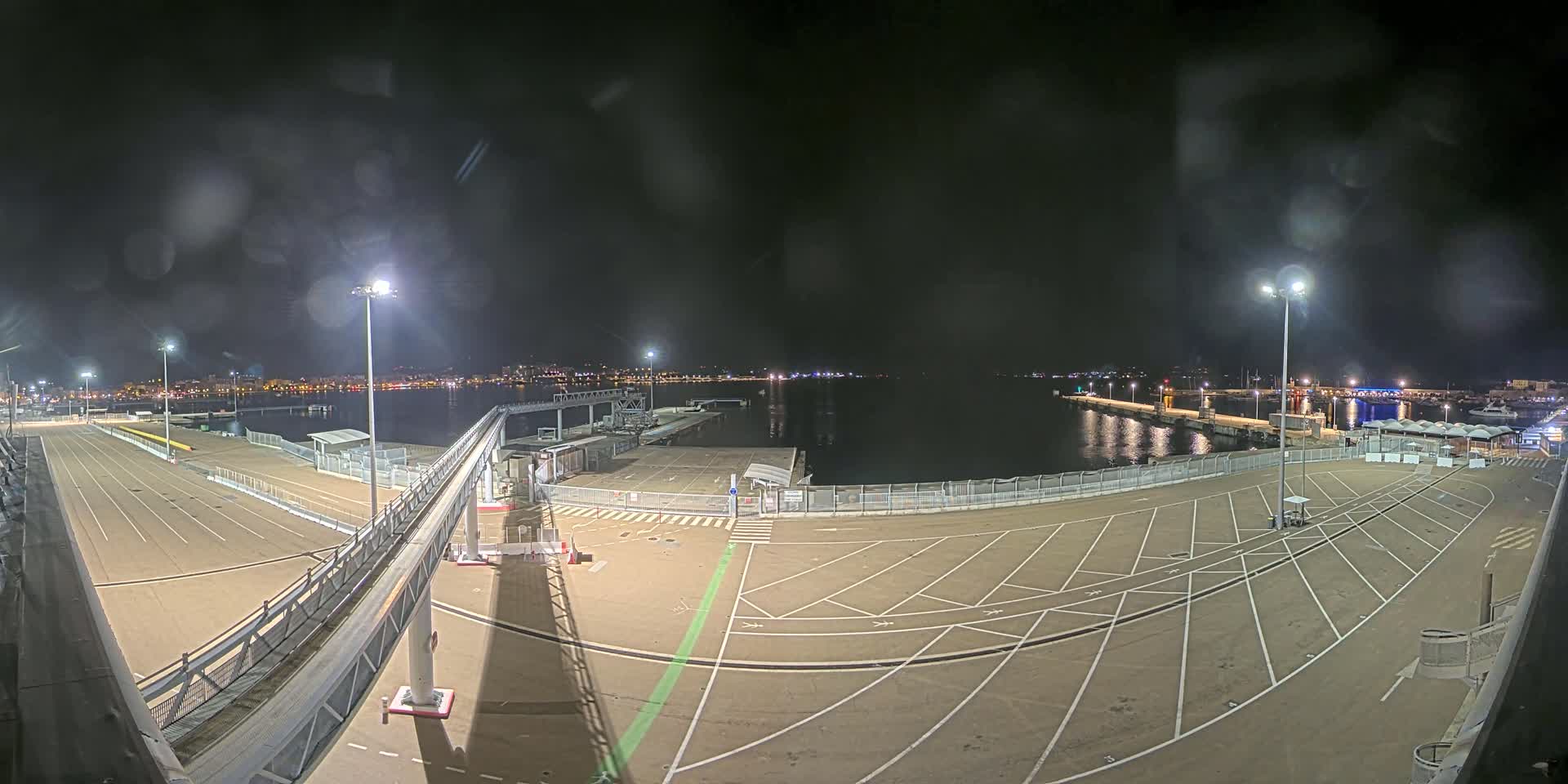 An empty, brightly lit port at night with a calm body of water in the background, viewed from an elevated position.