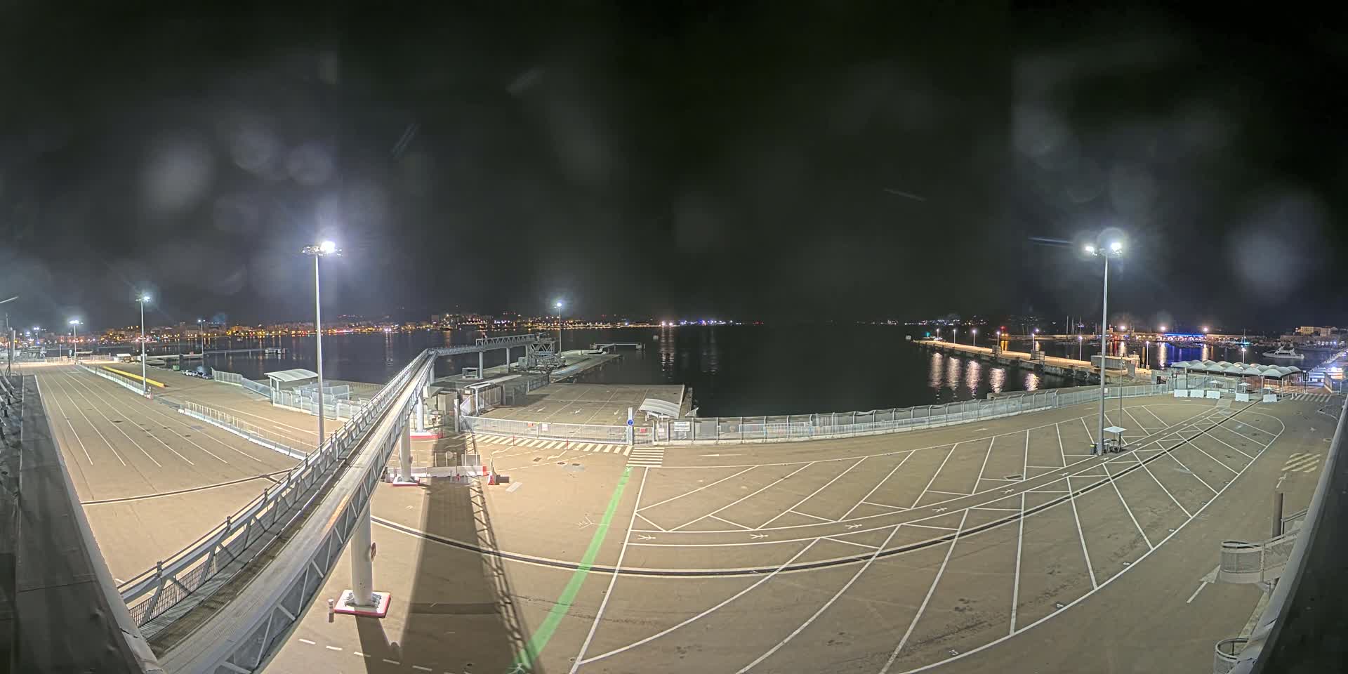 A nighttime view of an empty port with a long gangway and marked parking spaces, under a dark, slightly hazy sky.