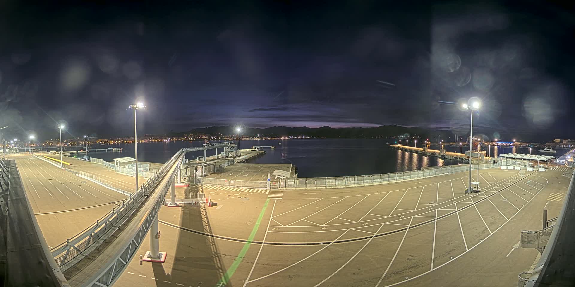 An empty, nighttime port with a walkway leading to a dock, under a slightly cloudy sky.