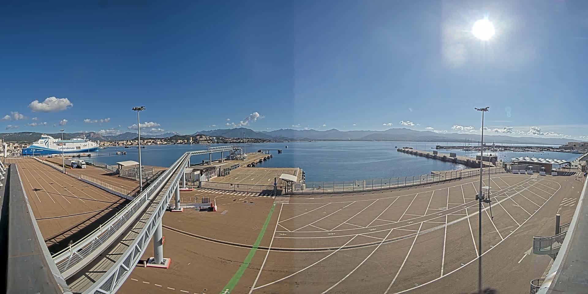 A ferry is docked at a port on a sunny day with a clear blue sky and mountains in the distance.