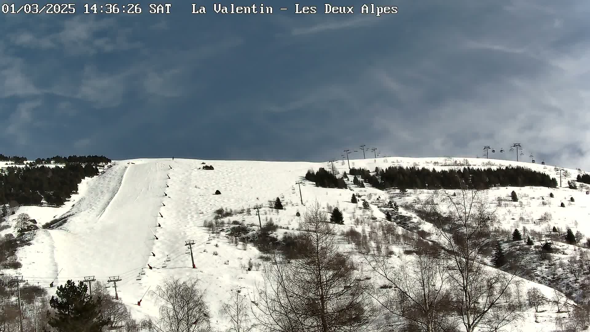 A snow-covered ski slope with sparsely wooded areas and several ski lifts under a partly cloudy sky.