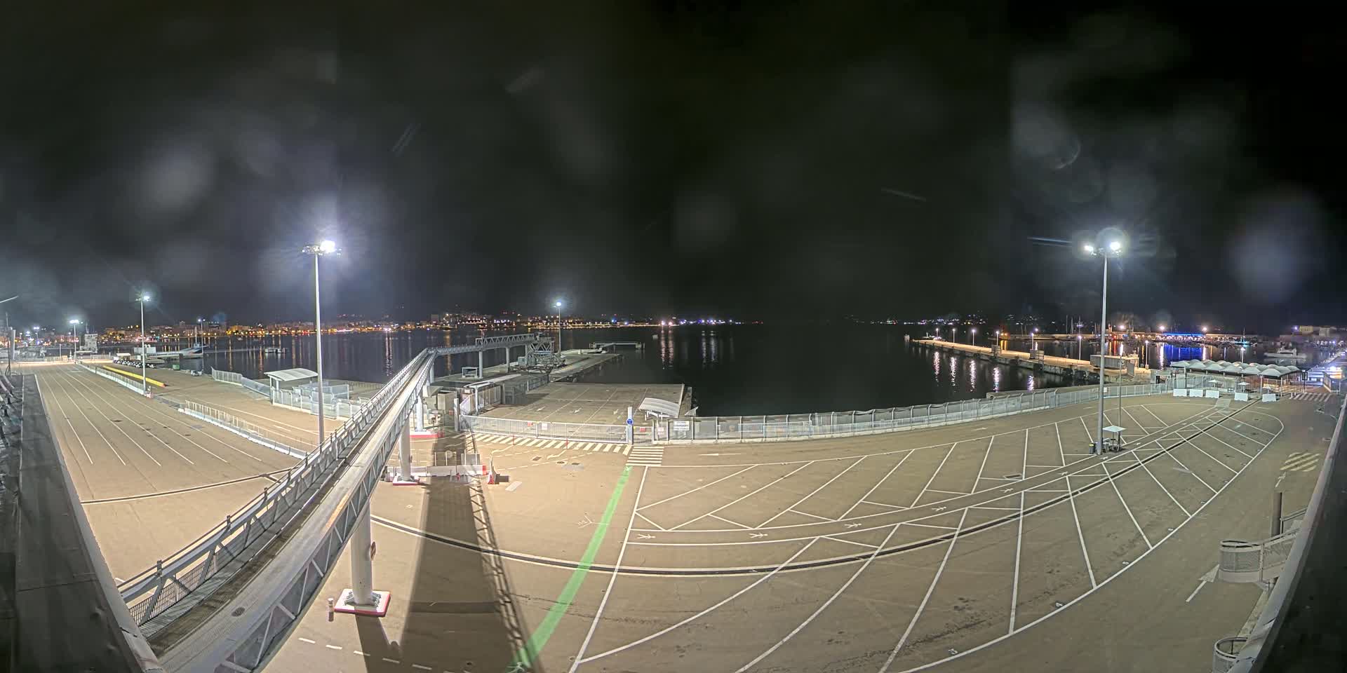 A nighttime view of an empty port area with a gangway and parking spaces, under a slightly cloudy sky.