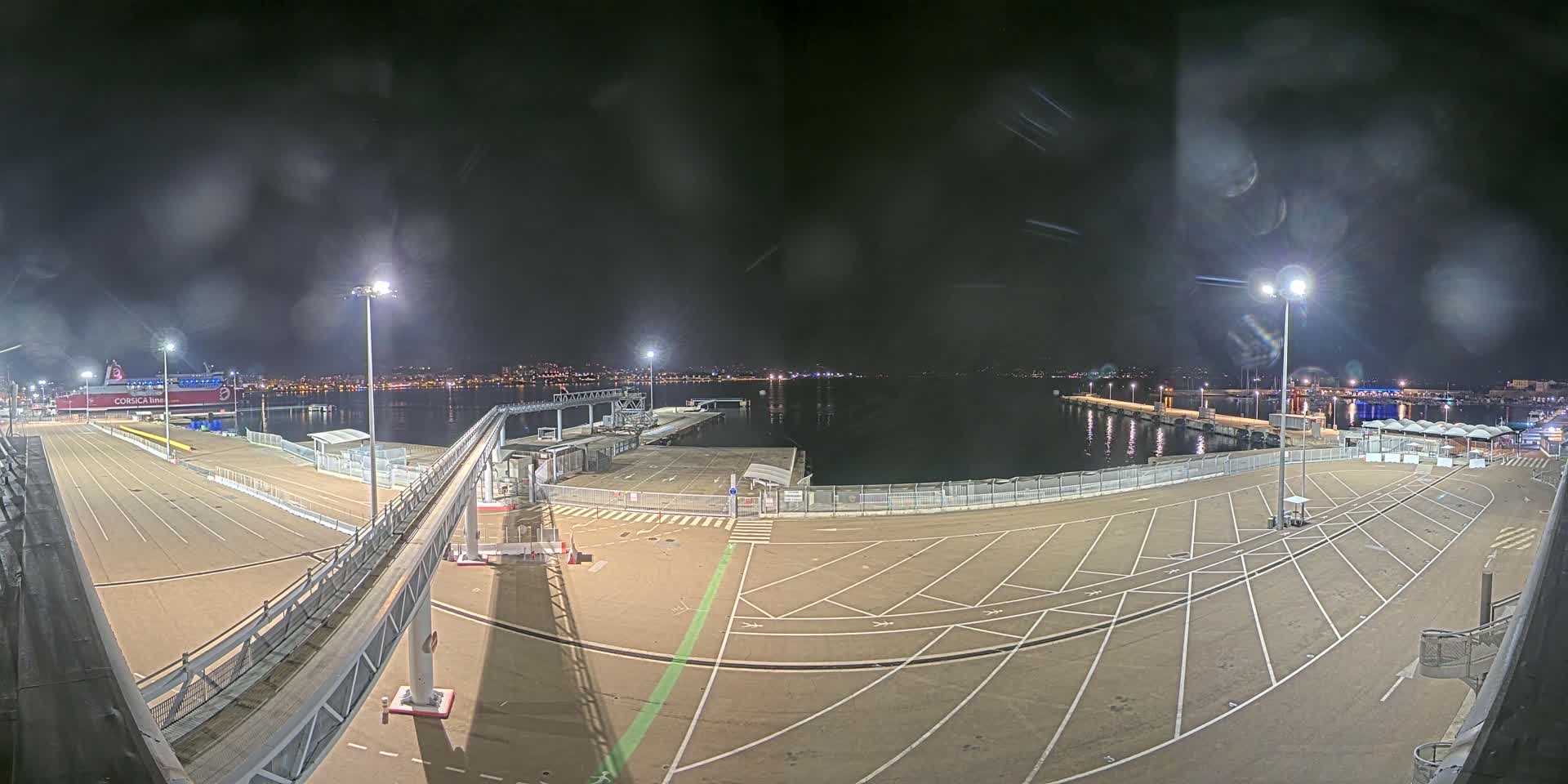 A nighttime view of an empty ferry terminal and docked ship, under a cloudy sky.