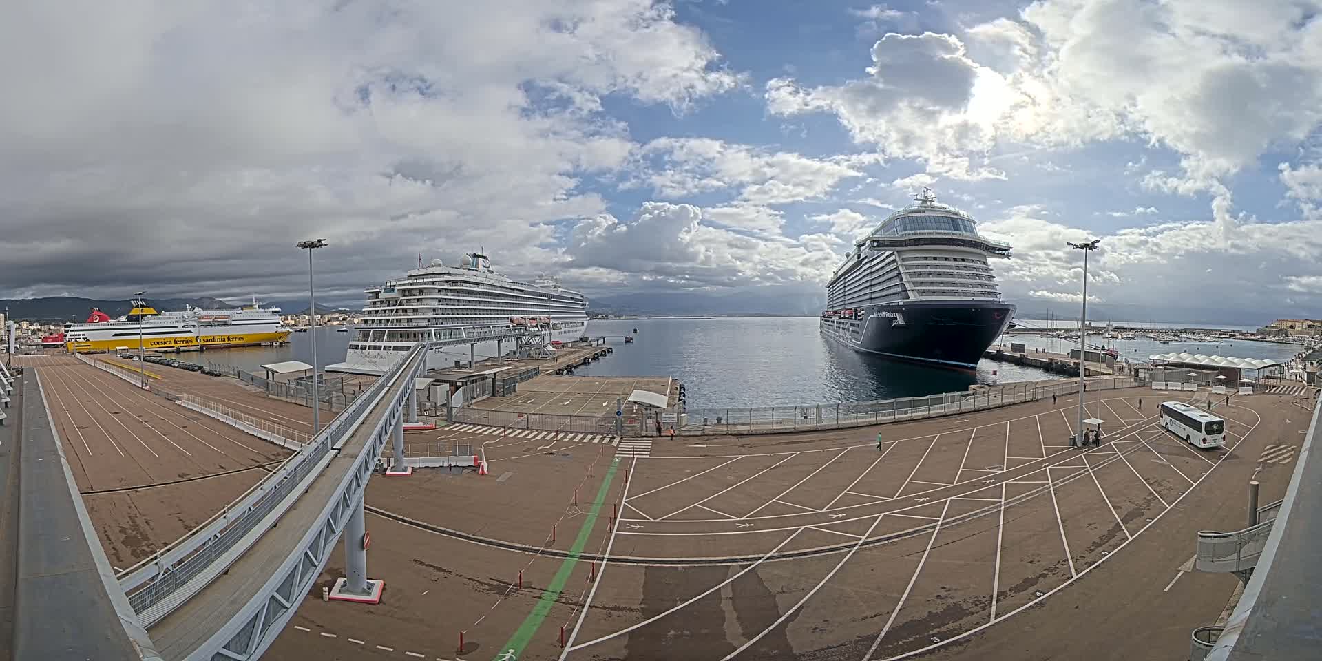 Two large cruise ships and a ferry are docked at a port under a partly cloudy sky.