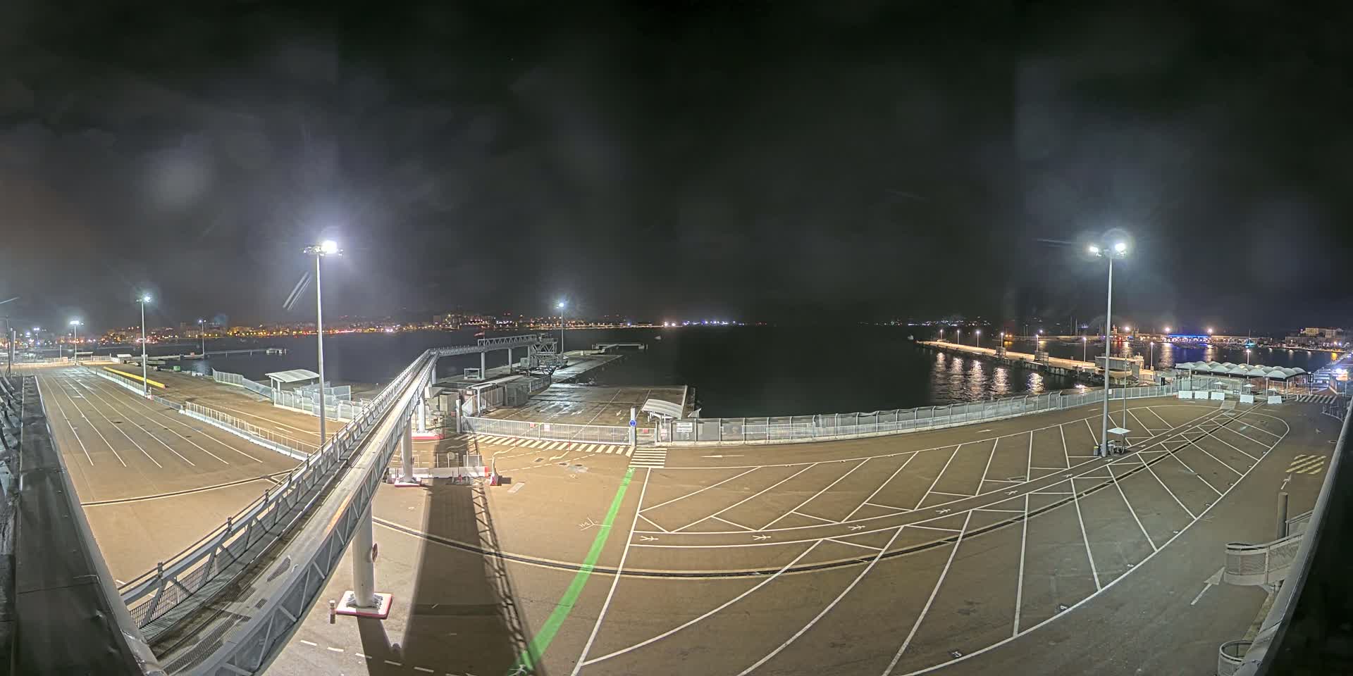 A nighttime view of an empty port with a gangway leading to a dark body of water under a slightly hazy sky.