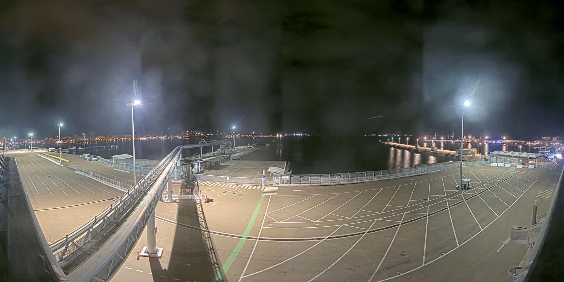 An empty, nighttime port with a long gangway leading to a docked ferry, under a cloudy sky.