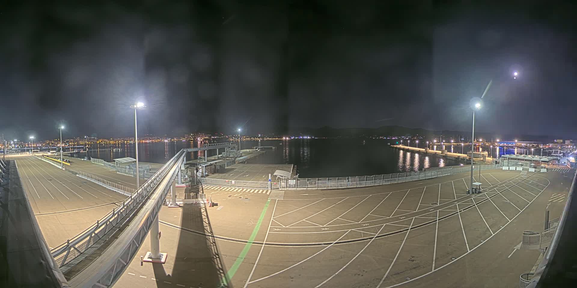 A nighttime view of a mostly empty port area with a gangway leading to a dock, under a dark, clear sky.