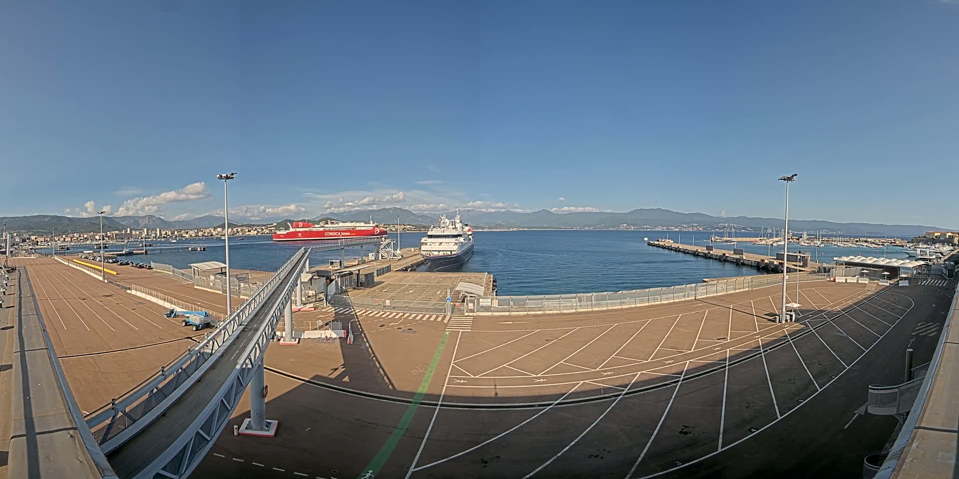 A mostly empty ferry terminal with two ships docked, under a clear blue sky.