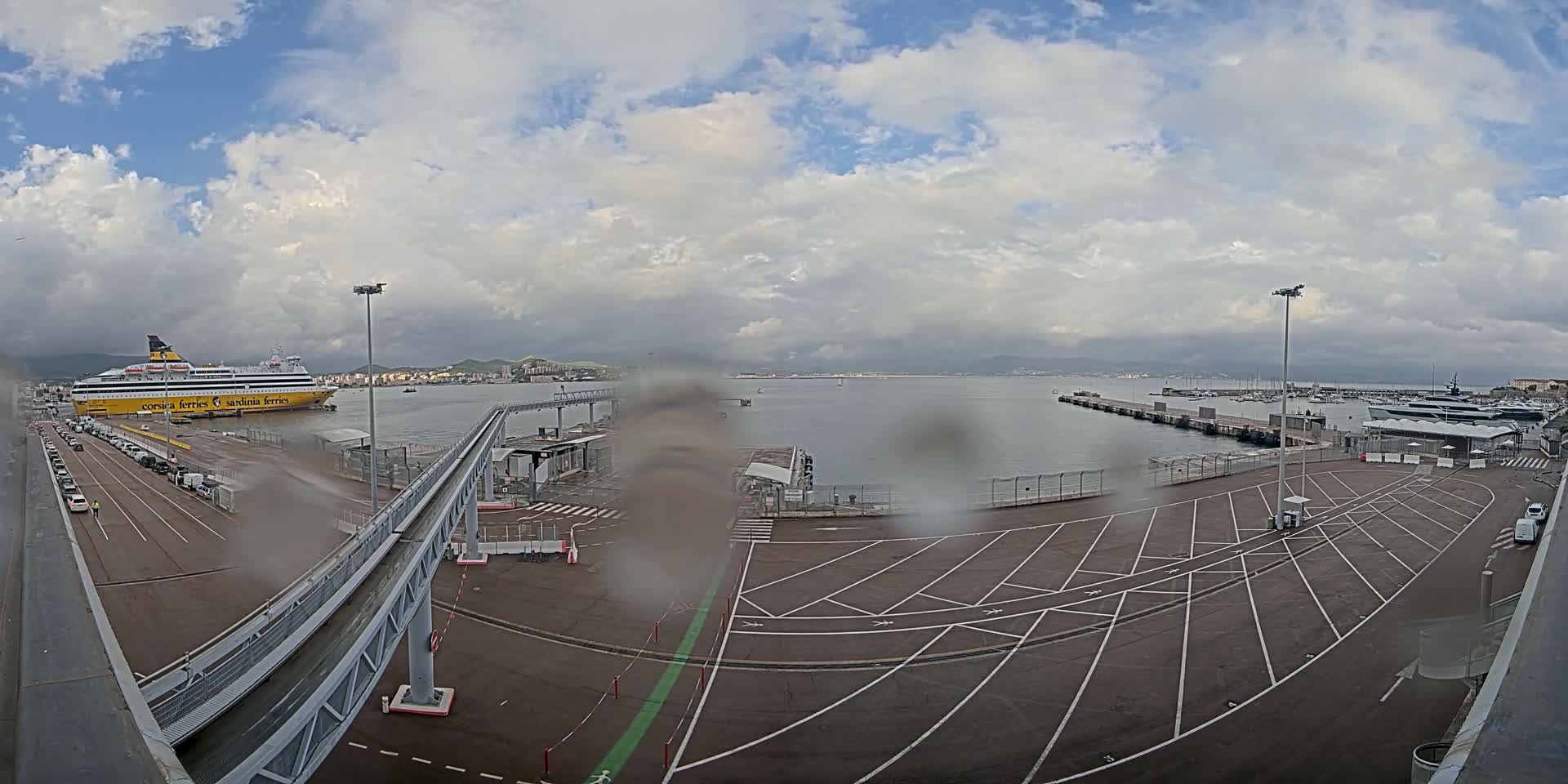 A large yellow ferry is docked at a port under a cloudy sky, with rain obscuring the view of the surrounding area.