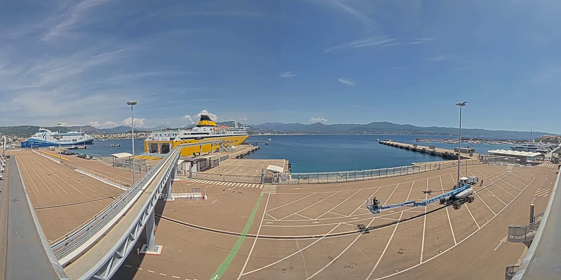 A large yellow ferry is docked at a port on a sunny day with clear skies, and another ferry is visible further down the pier.