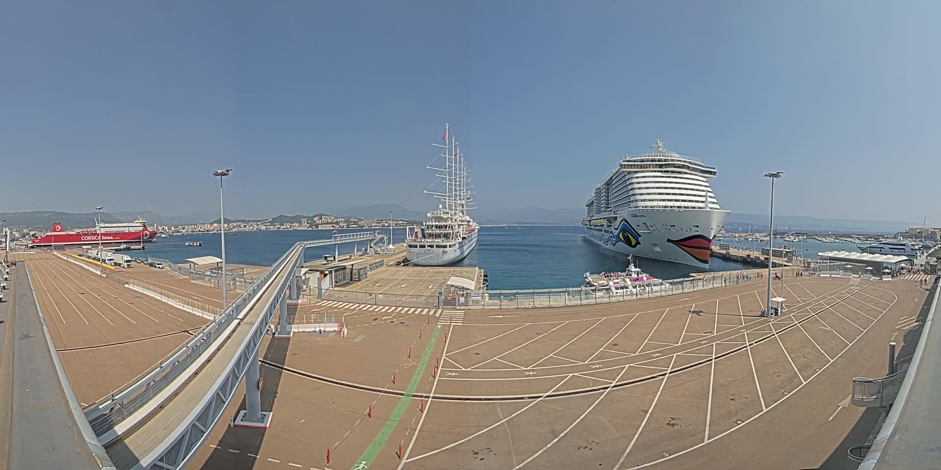 A port on a sunny day with three ships docked, including a large cruise ship, a smaller sailing ship, and a ferry.