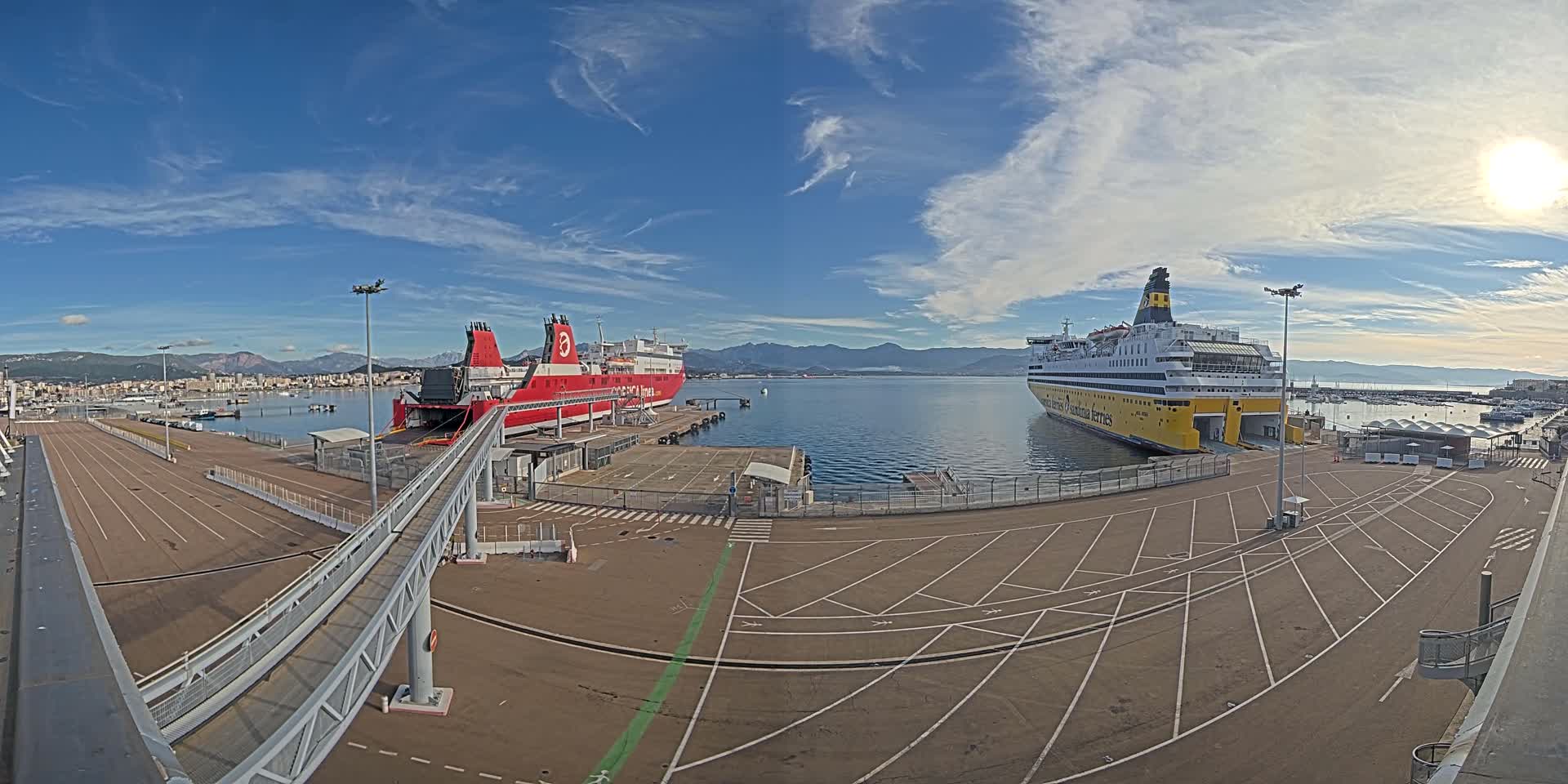 The image presents a harbor scene with a large yellow ferry, a prominent white cruise ship, and a distant blue ferry docked by concrete piers and access ramps, all illuminated by a bright sun breaking through an otherwise overcast sky.
