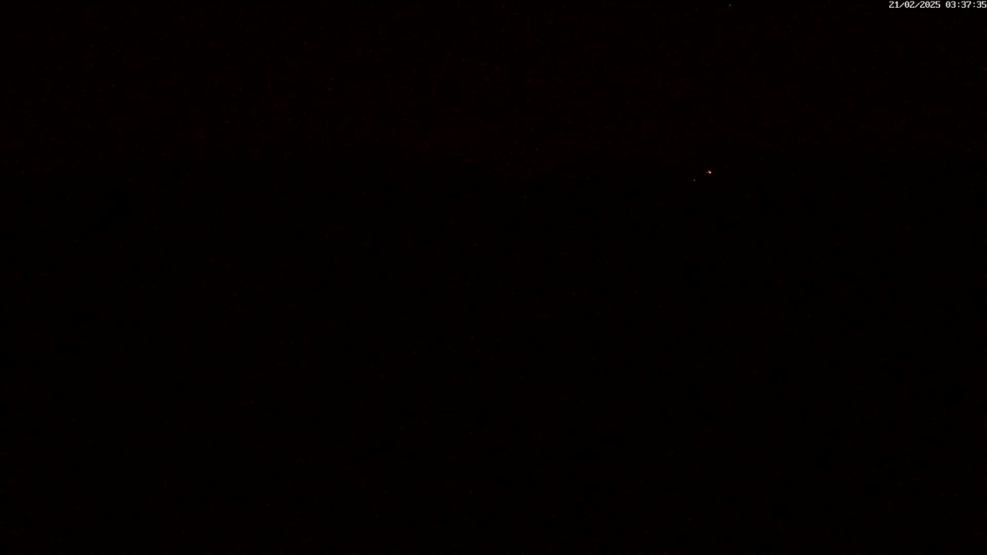 A mostly dark image with a small, faint light source visible in the distance under a nighttime sky.