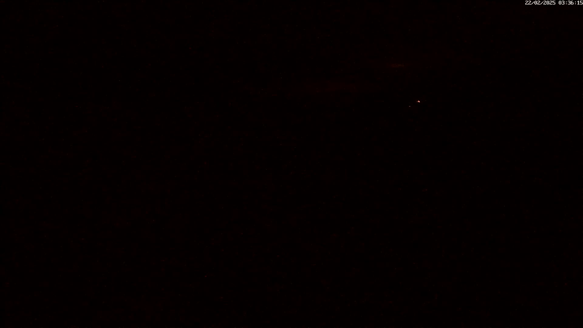 A mostly dark image shows a faint, reddish light in the distance under a dark night sky.