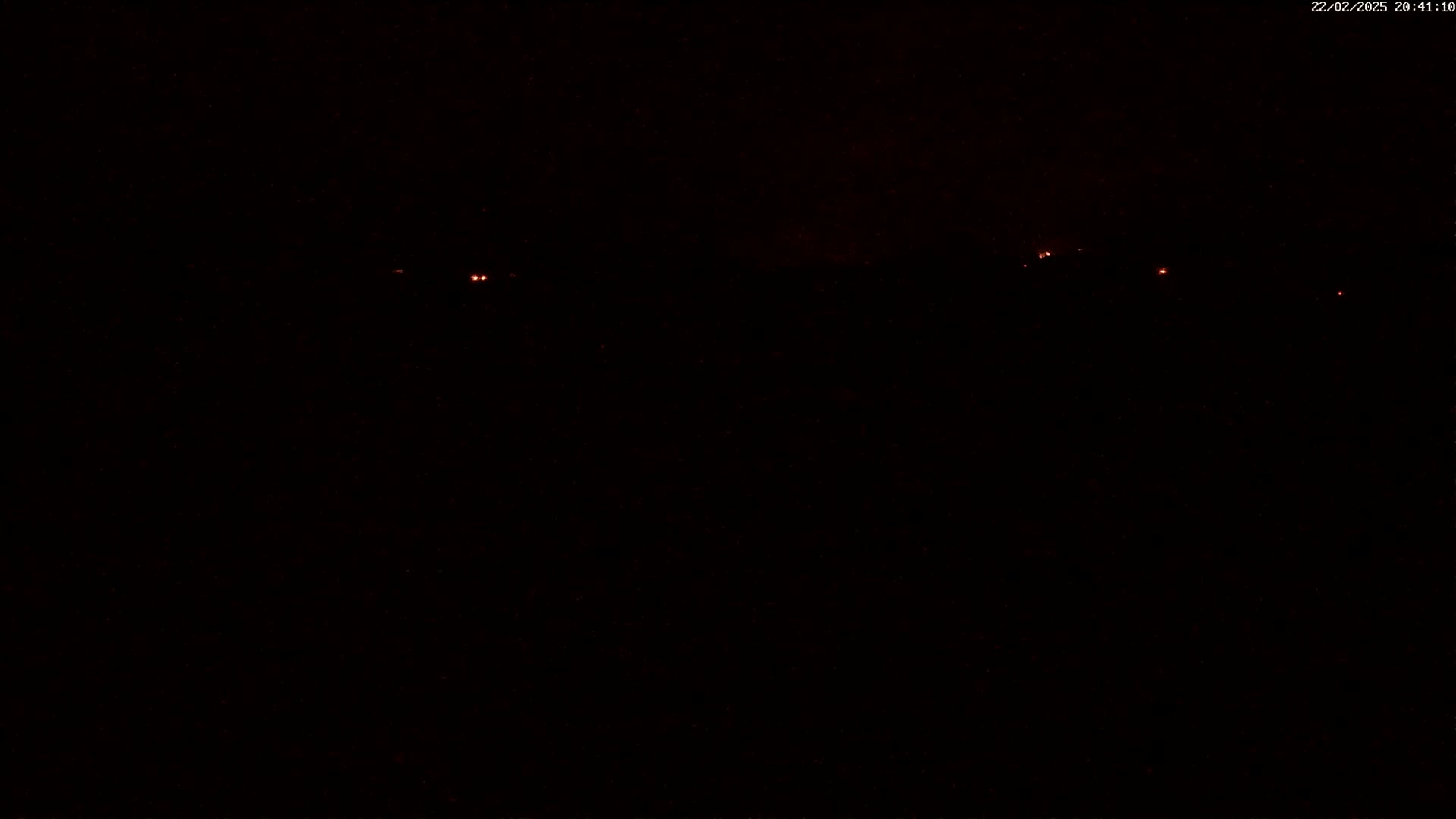 A dark, nighttime scene shows several small, distant red lights in the distance.