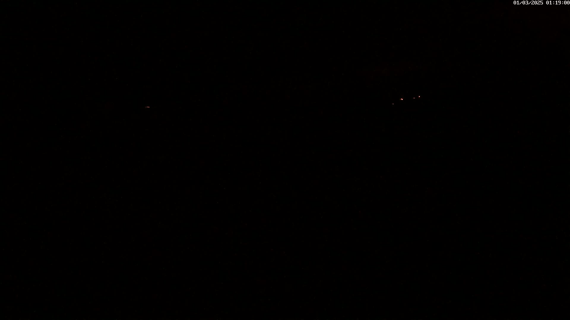 A nearly completely dark nighttime scene shows a few faint, distant red lights.