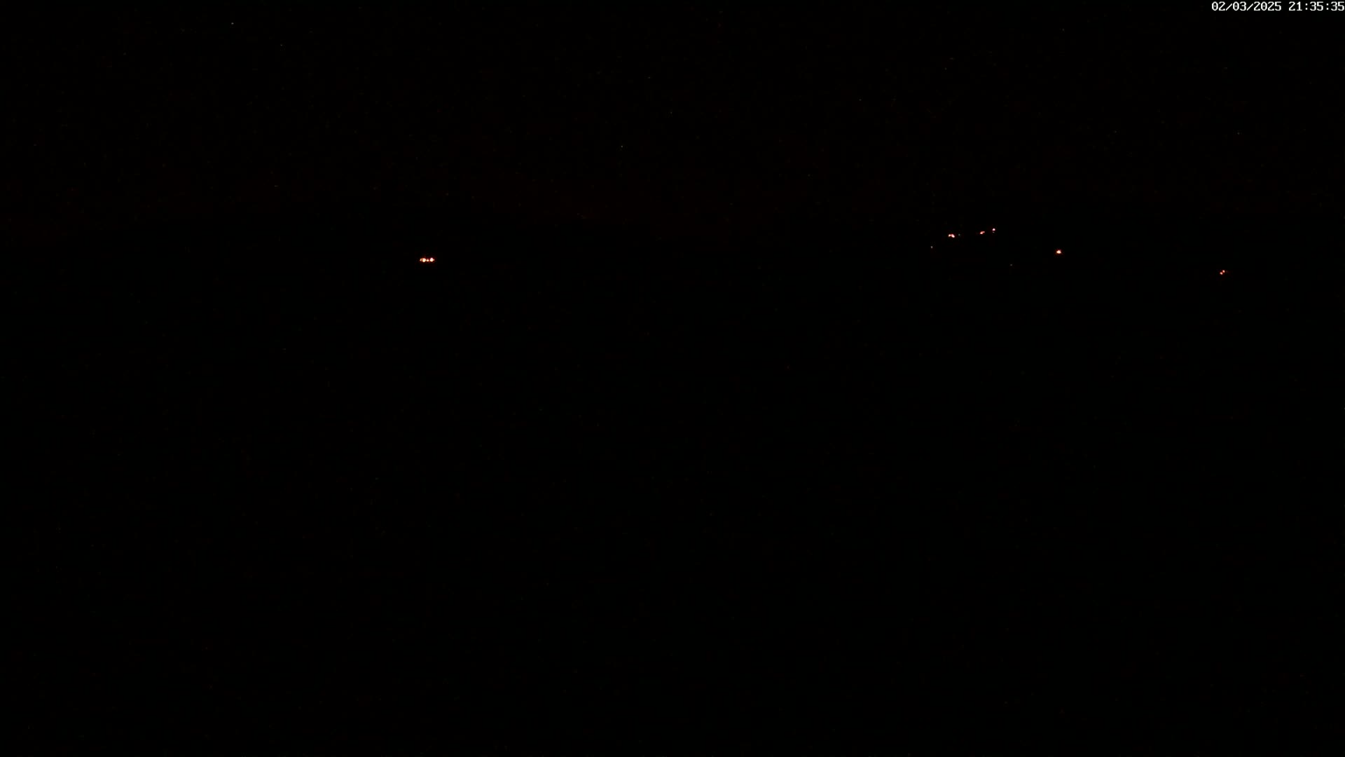 A dark, nighttime scene shows several faint, distant red lights.