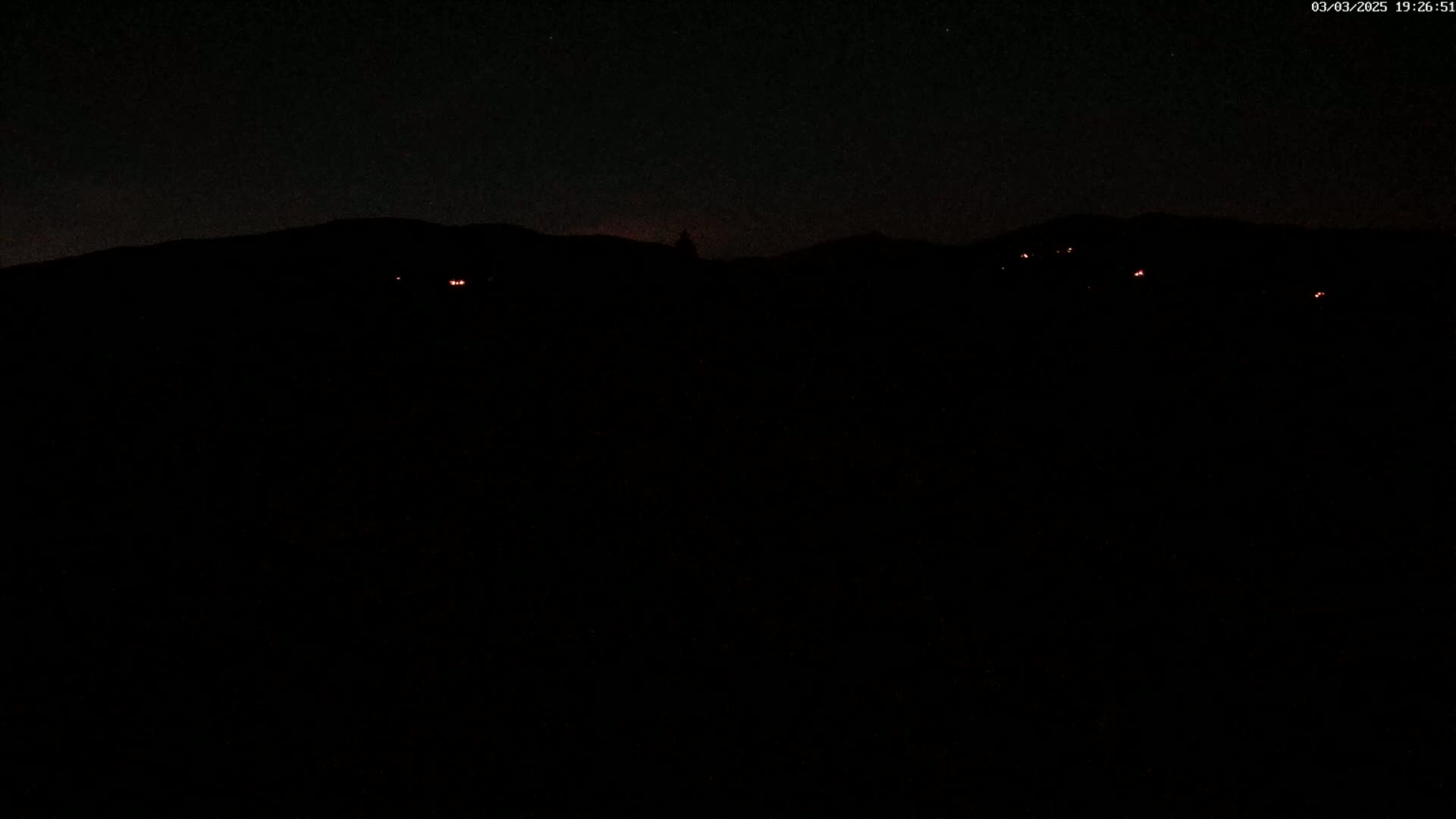 At night, several faint red lights are visible in the distance beyond a dark, silhouetted mountain range under a clear, dark sky.